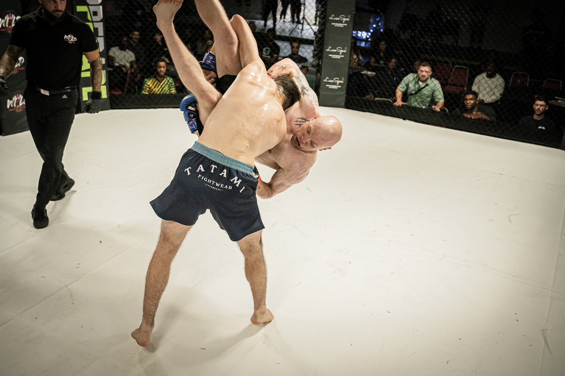 2 MMA Fighters fighting in a ring shot by a photographer. Guy being picked up and slammed to the ground.