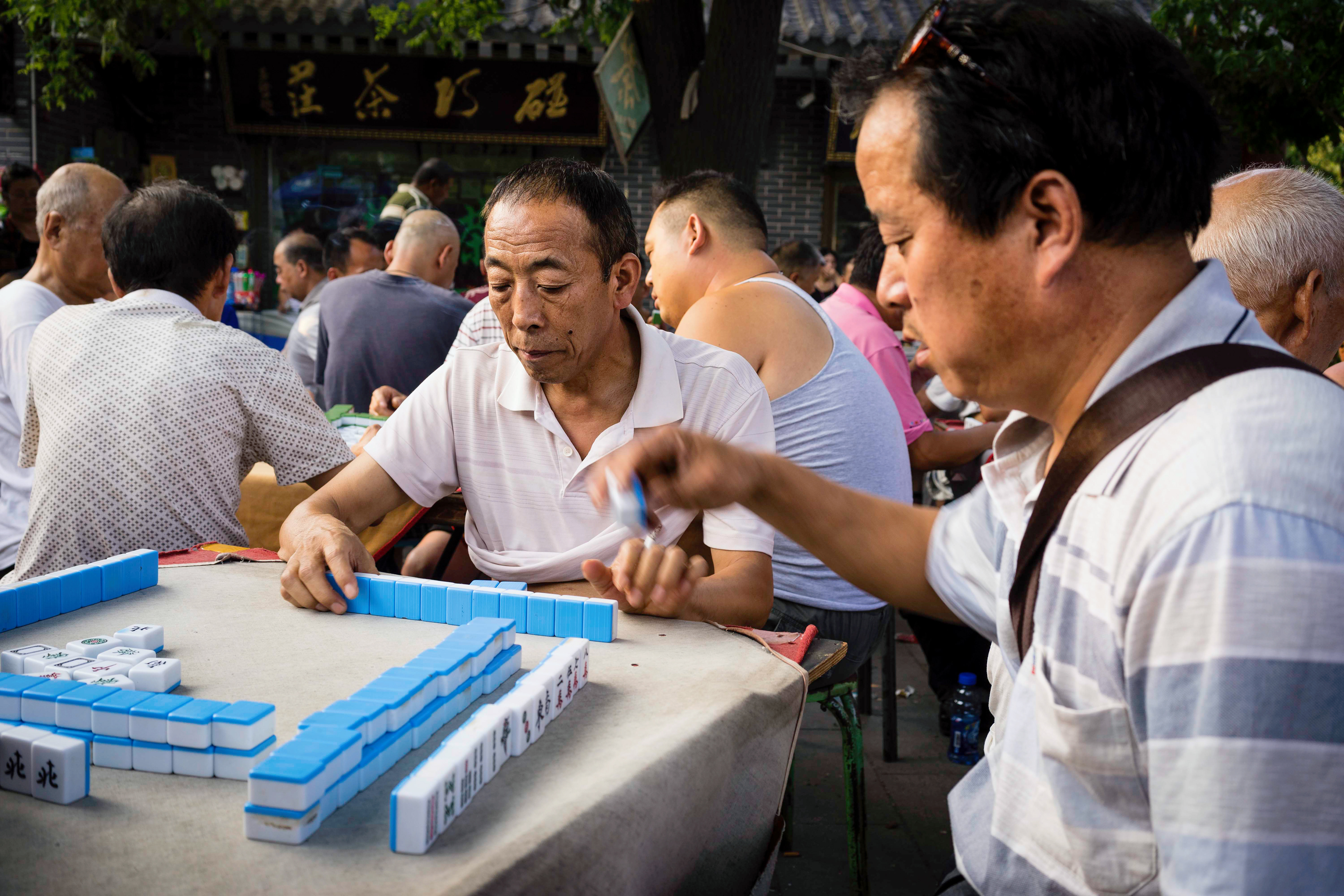 In the evening, after work, a large group of men gather just outside the city wall to smoke and play Mahjong. Xi'an, China.