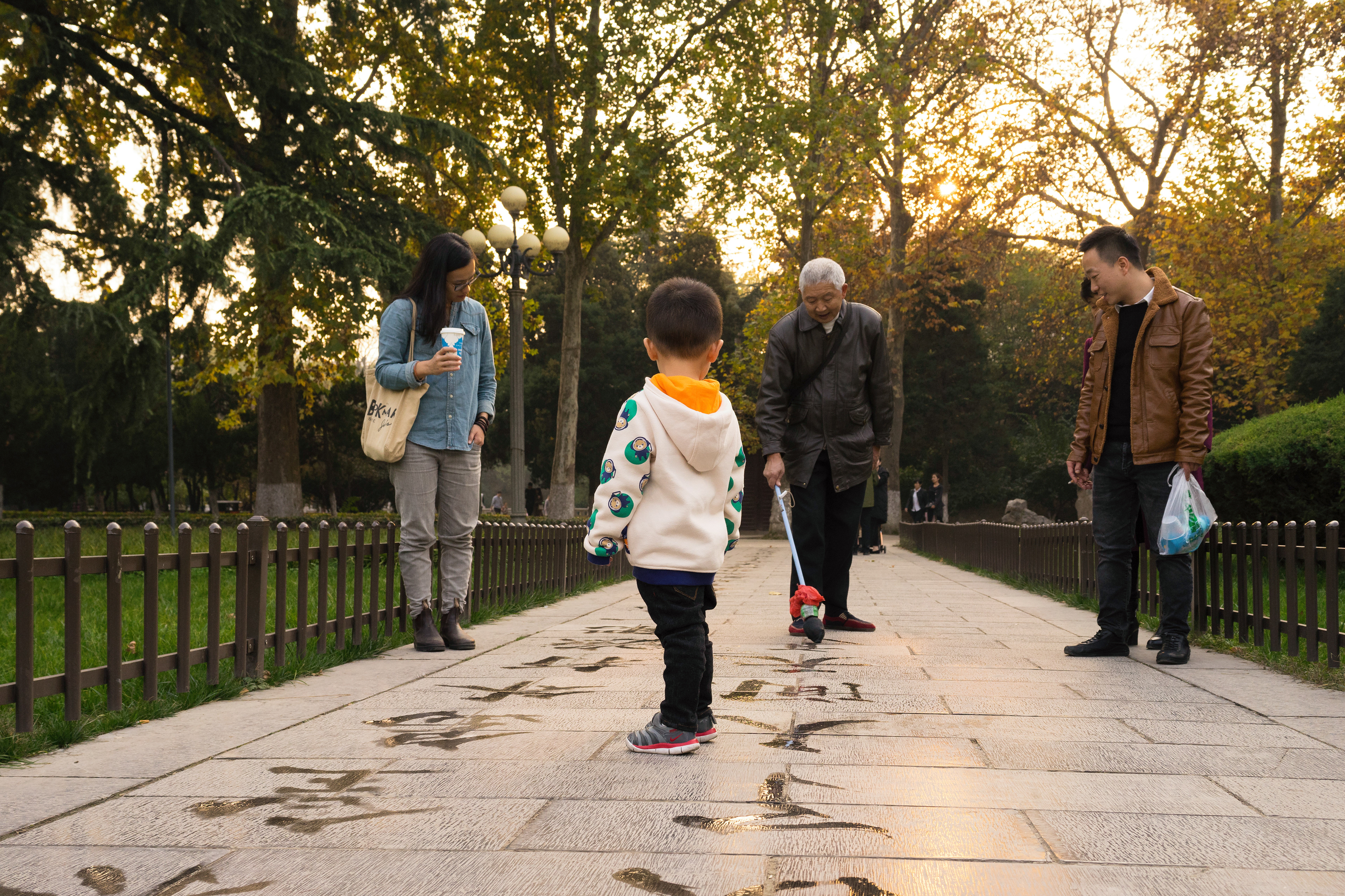 An elderly man draws a crowd with his calligraphy. He writes one of Mao’s poems, from memory, with a brush and water.