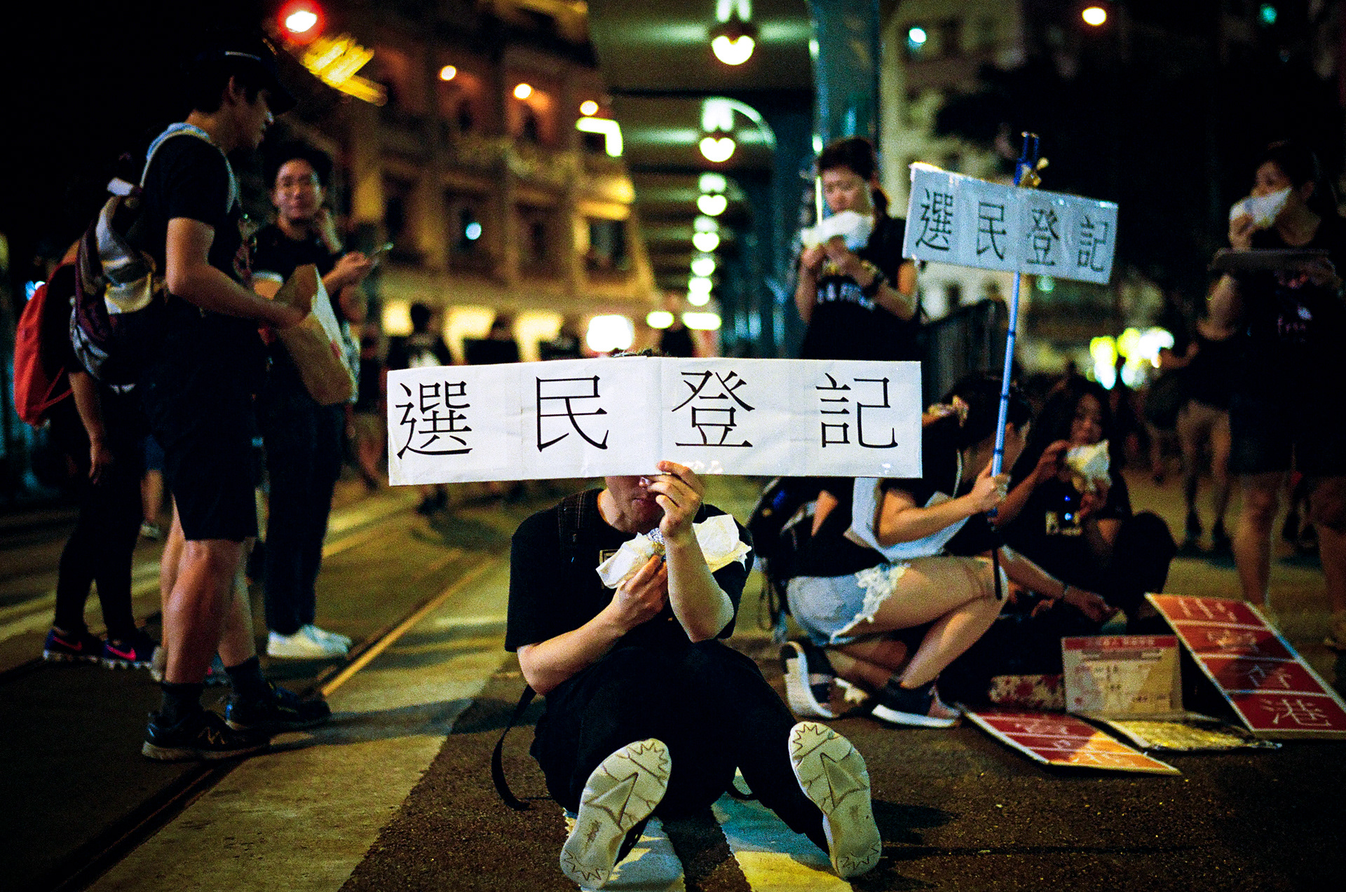 Admiralty, Hong Kong: Even while on a snack break, this protestor keeps his sign prominantly displayed. The sign reads simply: "Register To Vote" Hong Kongers took to the streets on Sunday, to push for the eradication of a proposed extradition bill that would have seen Hong Kongers arrested in the Special Administrative Region extradited to China. The bill was officially “suspended” by the Hong Kong’s Chief Executive Carrie Lam on Saturday. June 16, 2019 - Hong Kong, 35mm