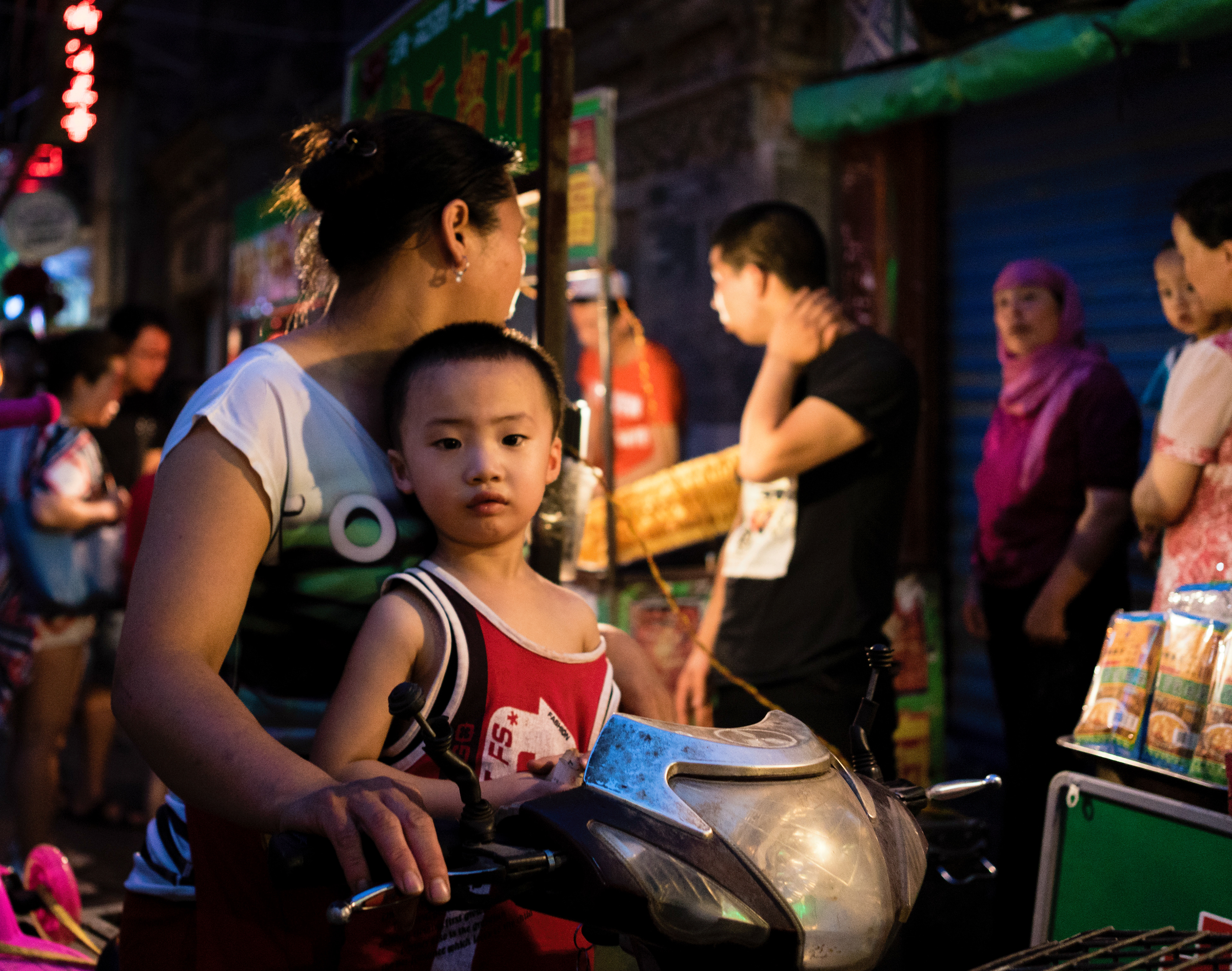 A young boy sits with his mother in the night market of the Muslim Quarter. Xi'an, China.