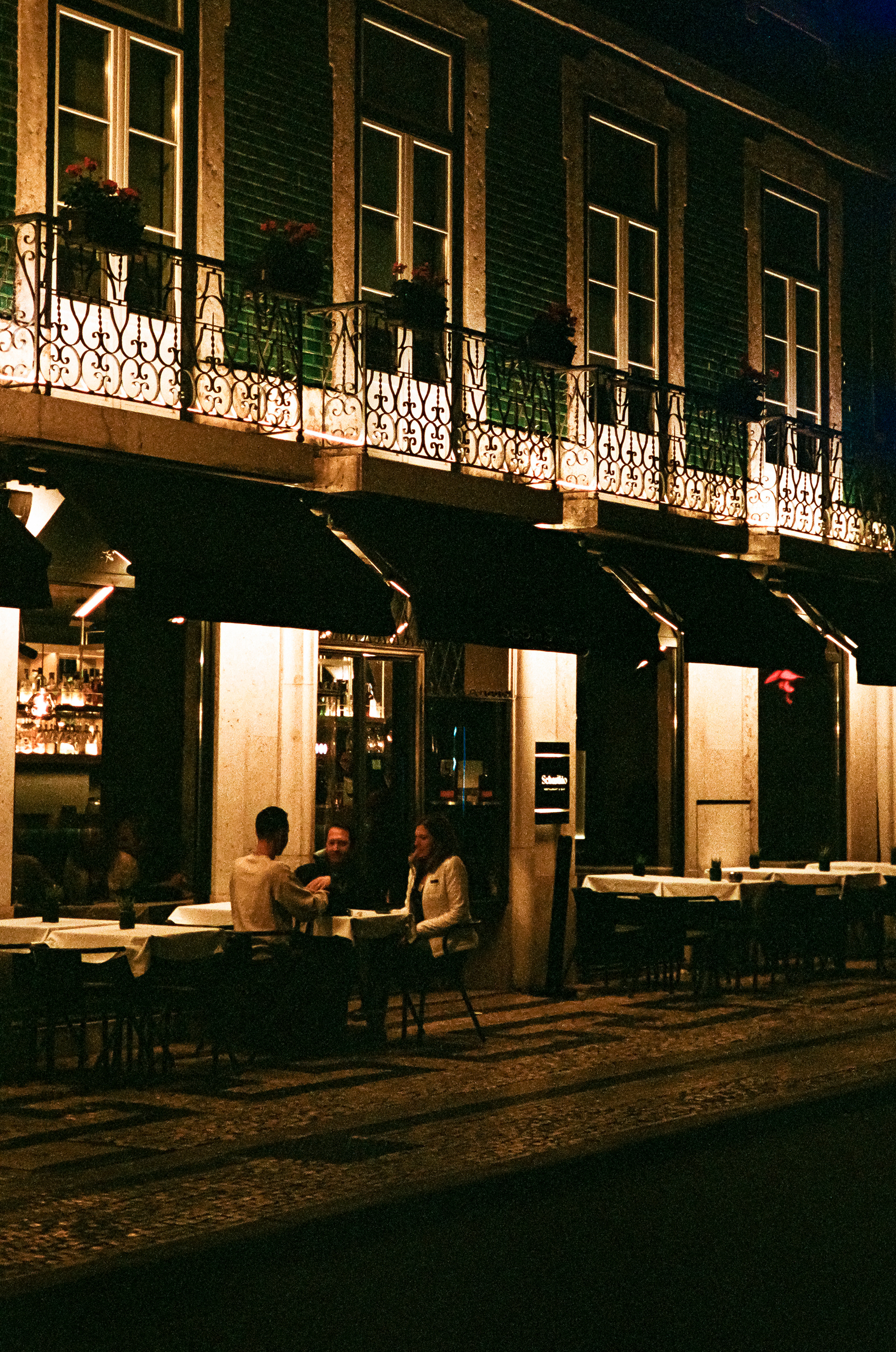 Dinner Together: A family enjoys dinner on a quiet street in Lisbon. Portra 400 pushed to 800.  April 1, 2023-Lisbon, Portugal-Photo by Aaron Guy Leroux