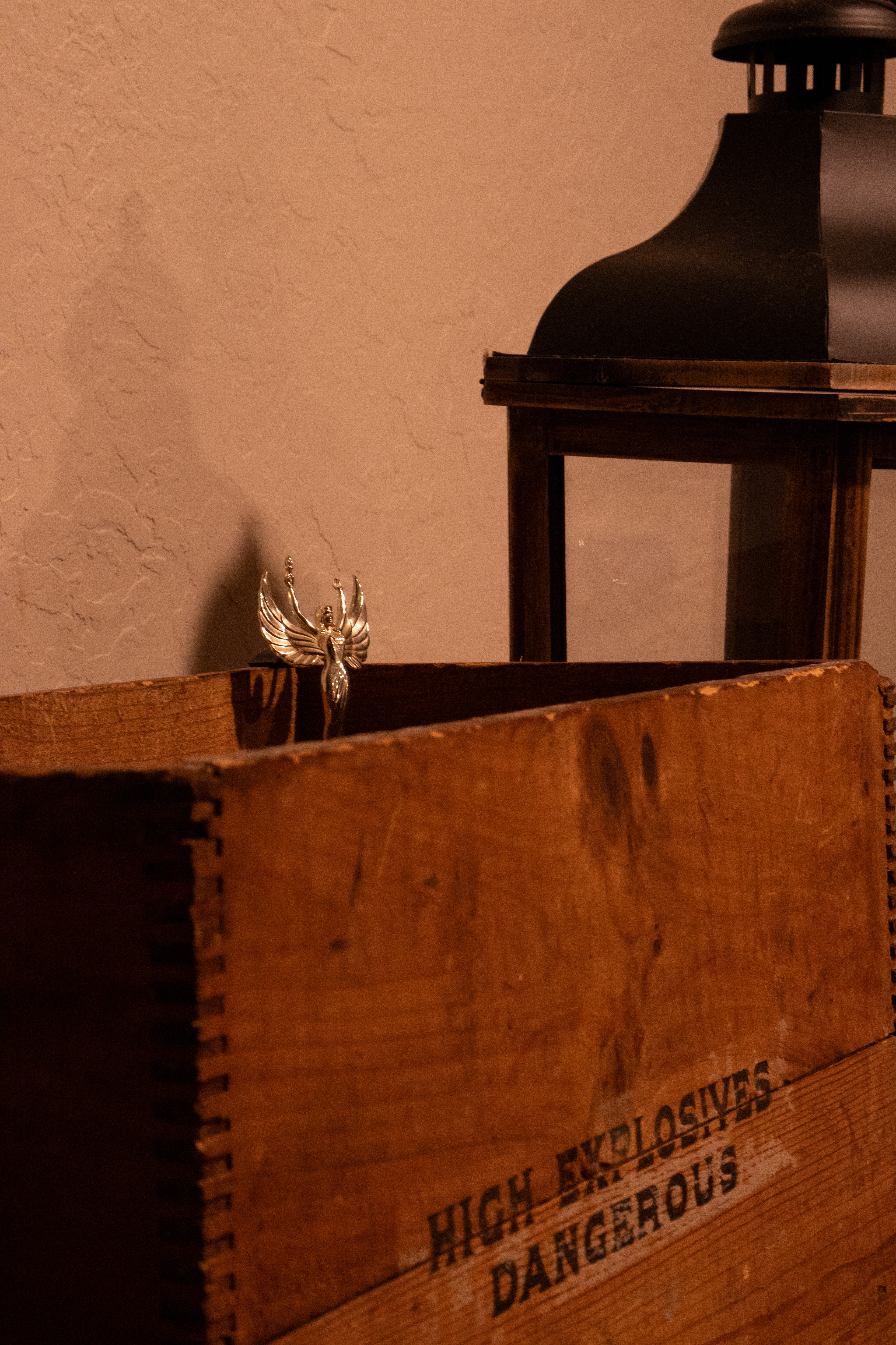 High Explosives Dangerous wooden crate with a golden angel trophy inside by a candle lamp.