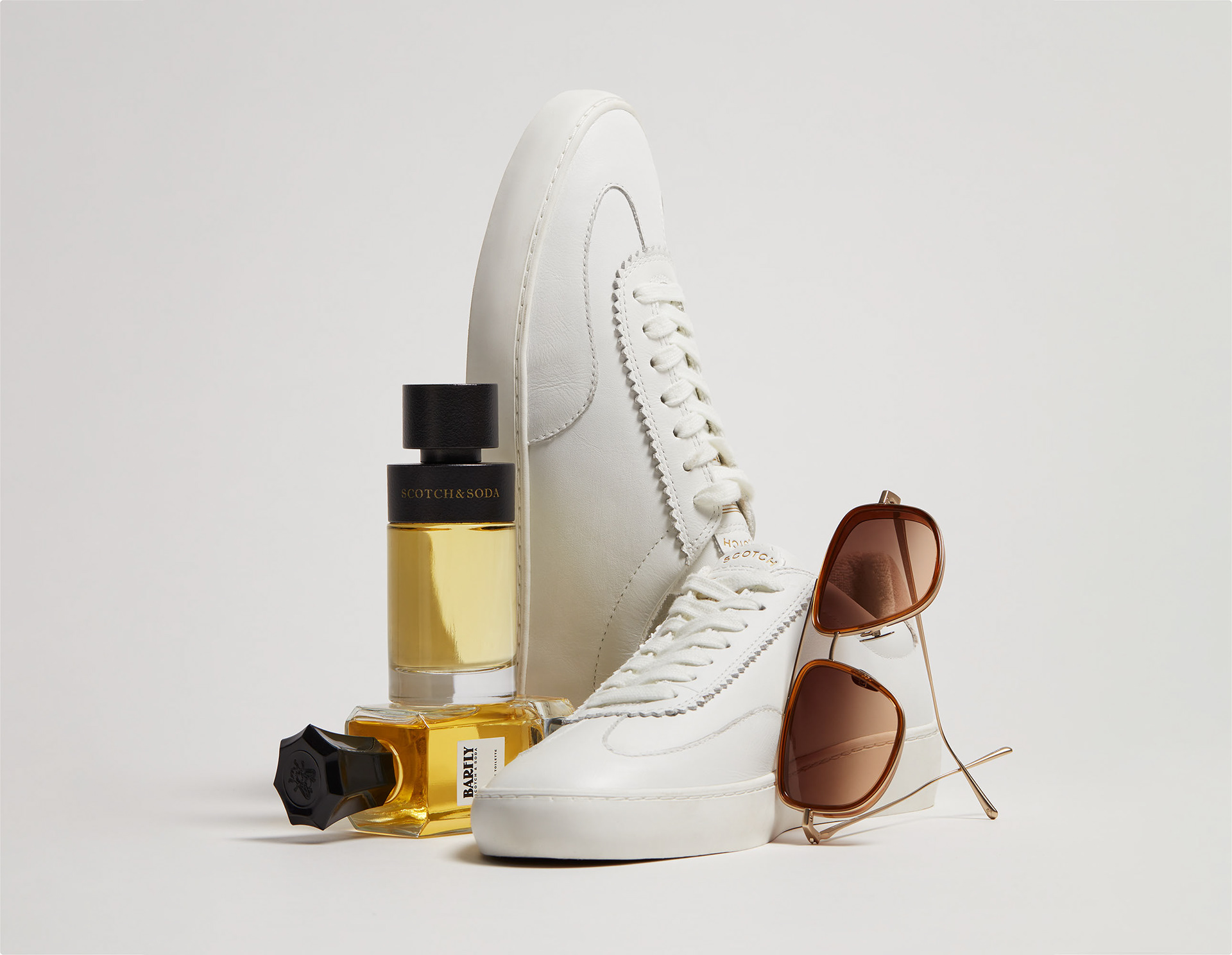 Ecommerce still life picture on white sneakers, parfume bottles and brown sunglasses displayed in a triangle shape
