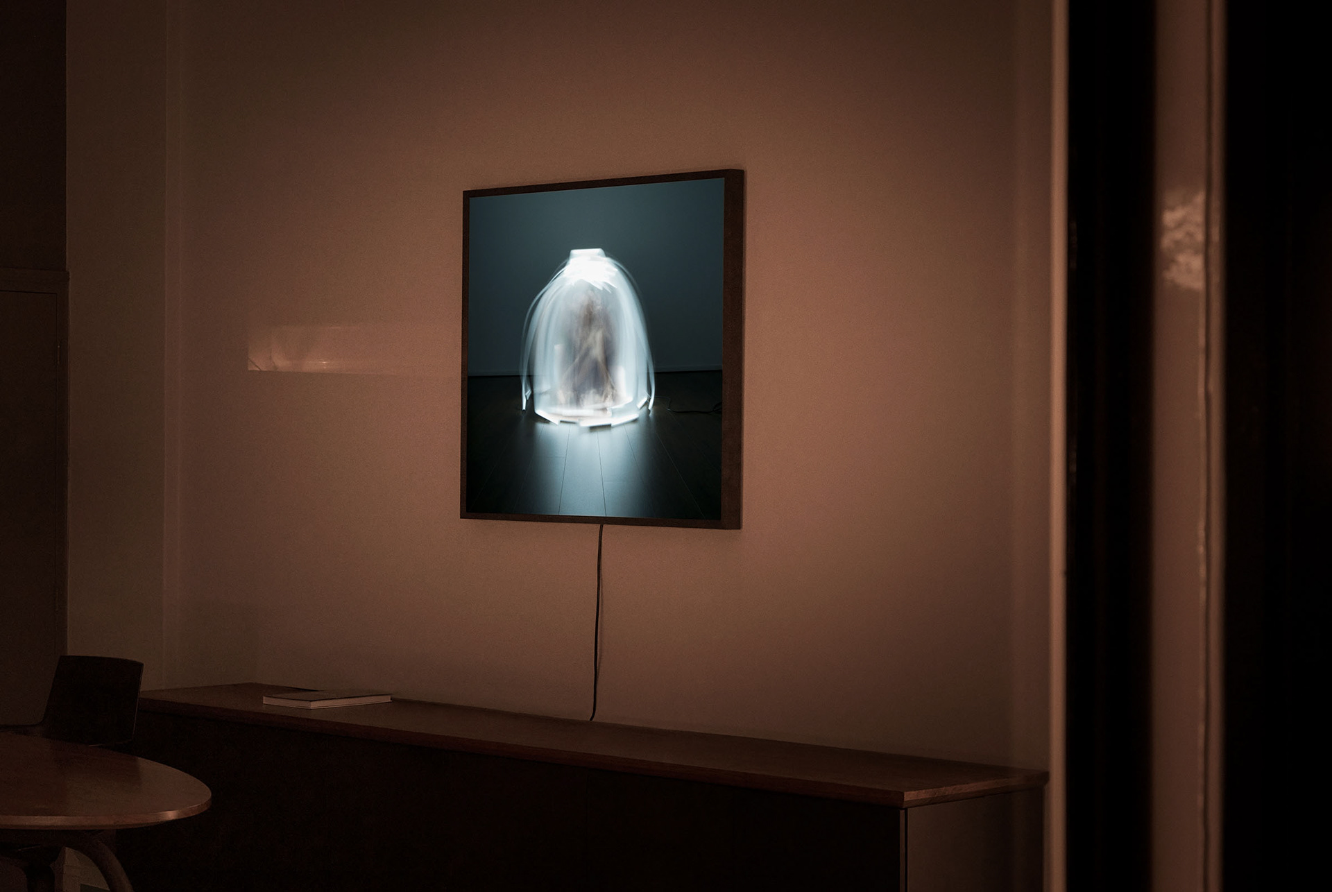 installation picture taken at night from outside looking into a gallery during an exhibition about light showing a lightbox with the work with the title firewall made by Pim Leenen