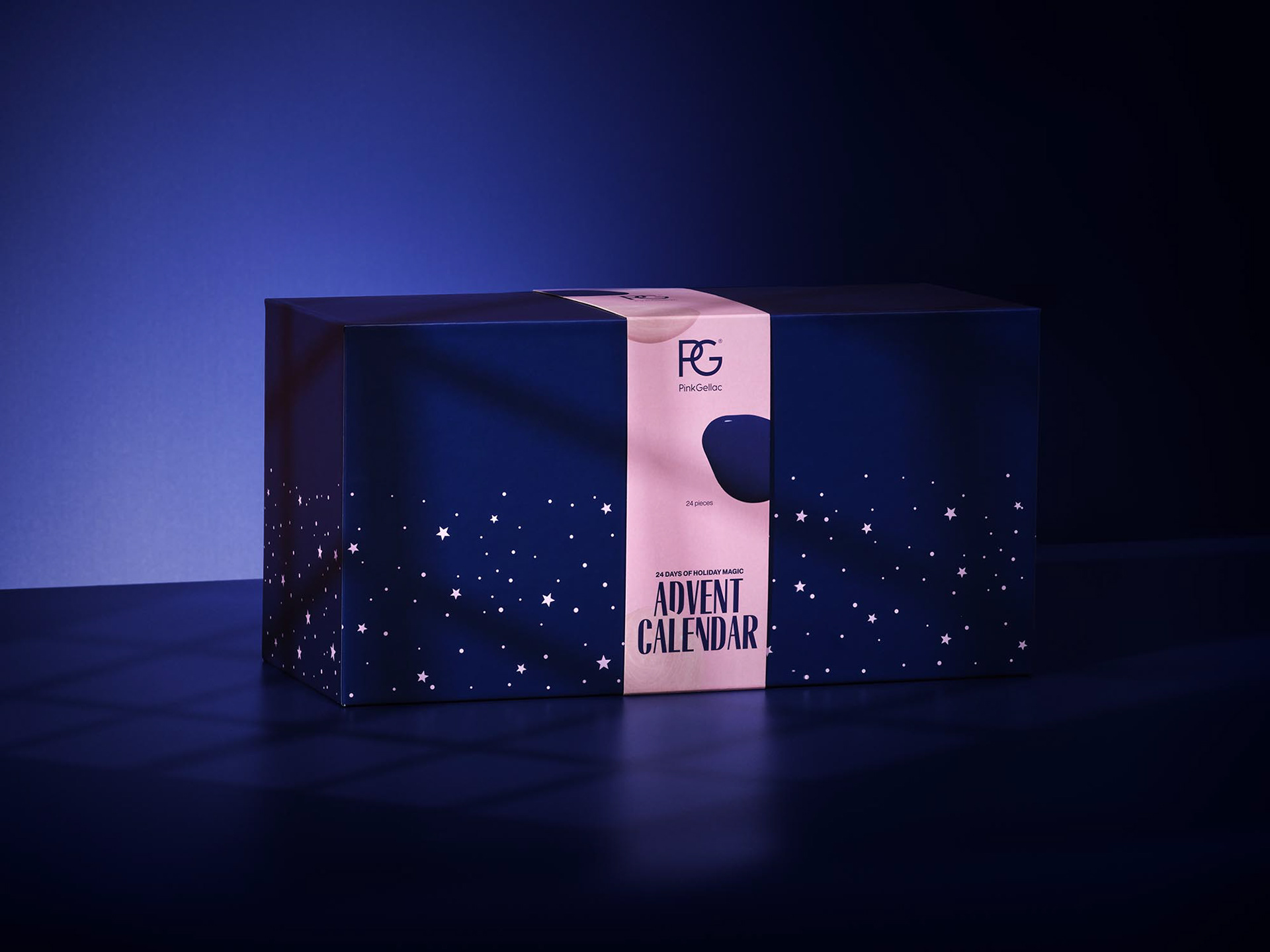 High-end product shot of a luxury advent calendar box by Pink Gellac, photographed in a minimalist studio setting with deep purple and magenta lighting. The box is dark navy blue, decorated with a subtle pattern of white stars and a soft pink paper band that wraps around the center, featuring elegant typography. The scene is bathed in soft shadows and gradient lighting, creating a dreamy, magical, and premium holiday atmosphere. The composition is clean and symmetrical, emphasizing sophistication and exclusivity.