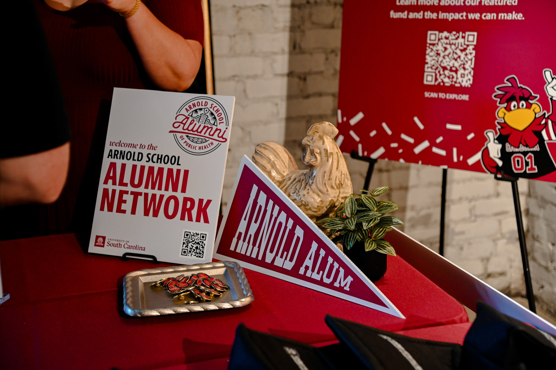 Sign with "welcome to the Arnold School alumni network" on a table next to lapel pins.