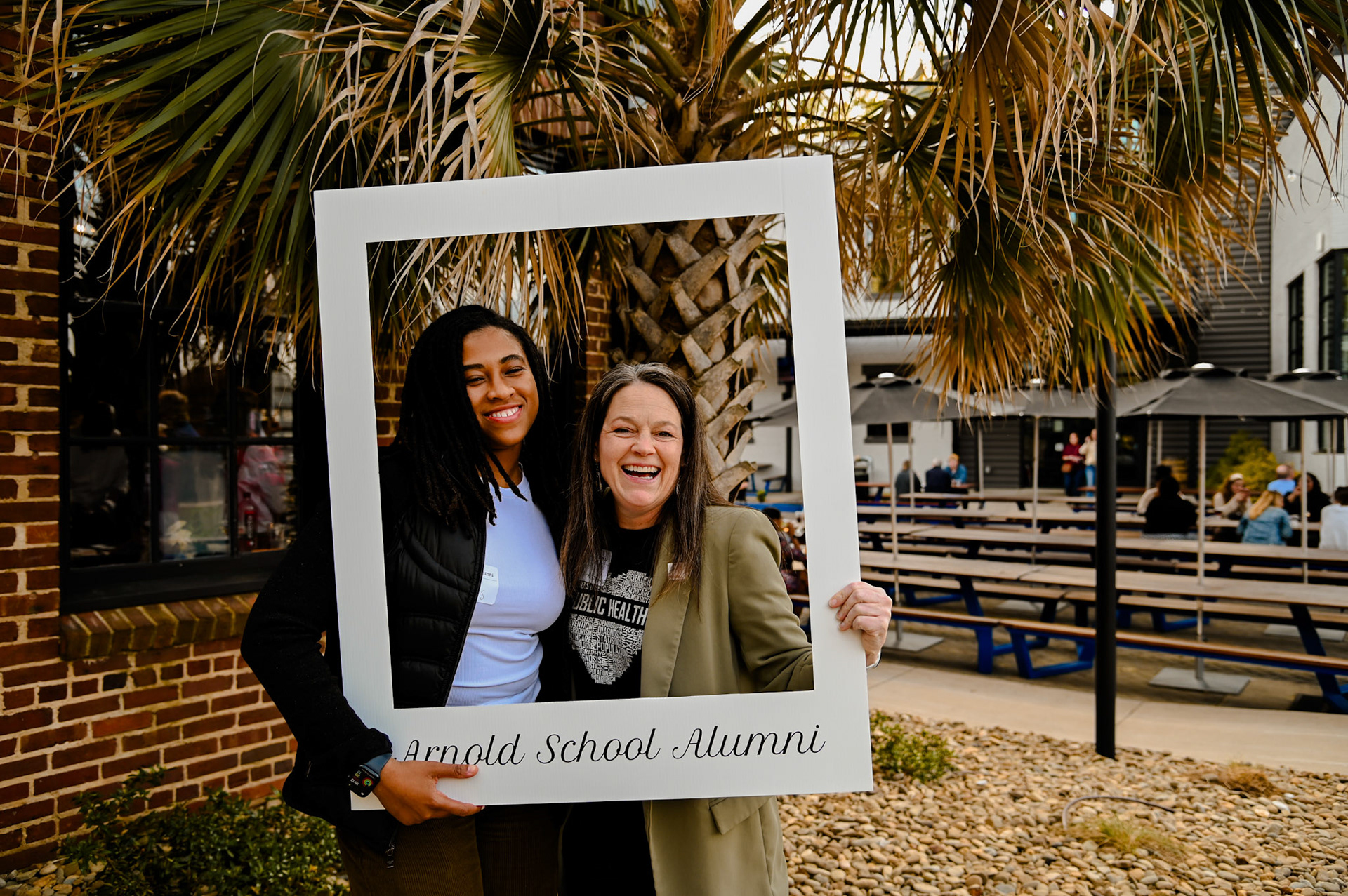 Brittany Sutton and Dean Sabo-Attwood posing with a large photo frame that says "Arnold School Alumni"