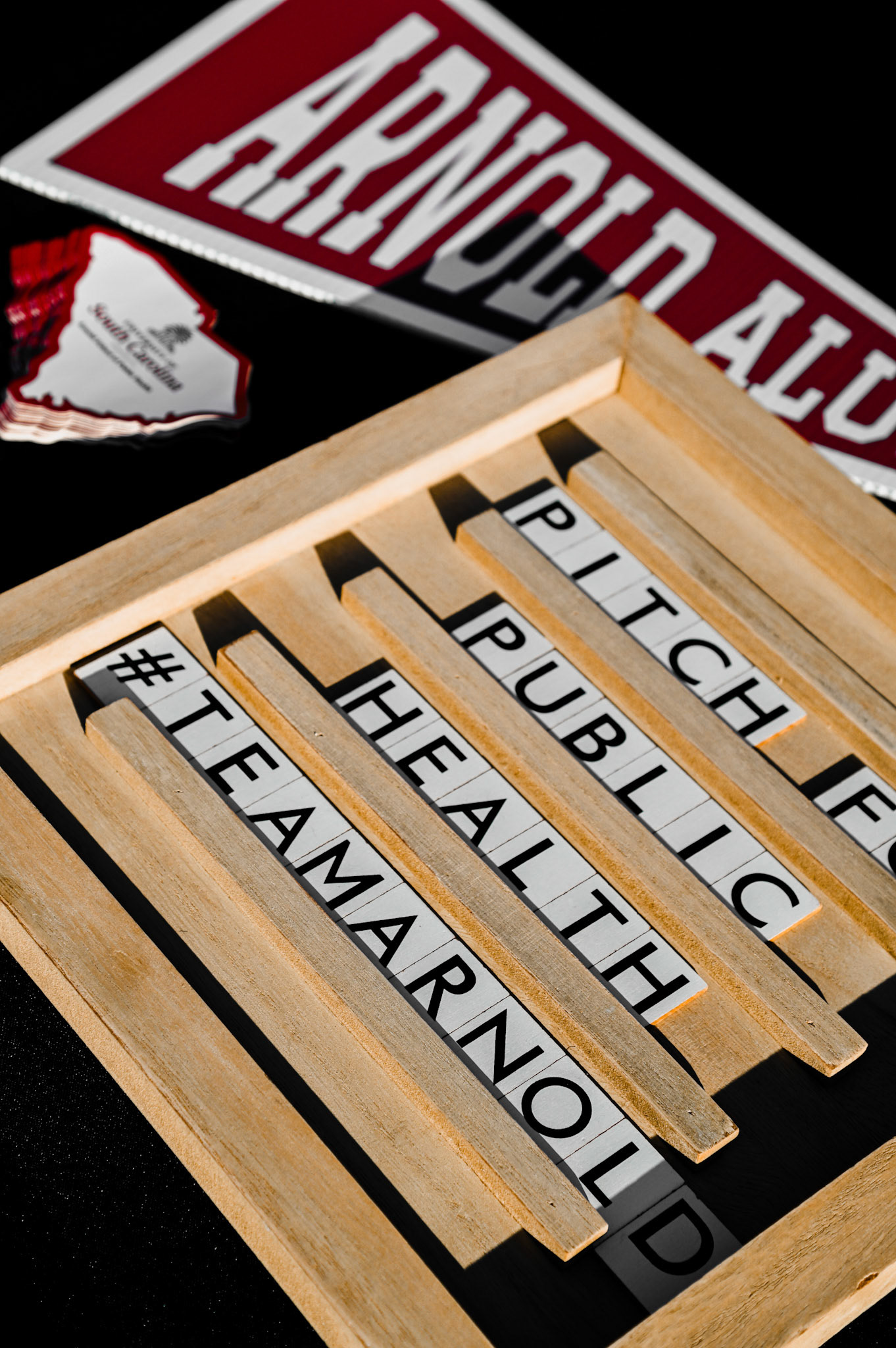 Block letters in a wooden container on a table, which says, "pitch for public health #teamarnold"