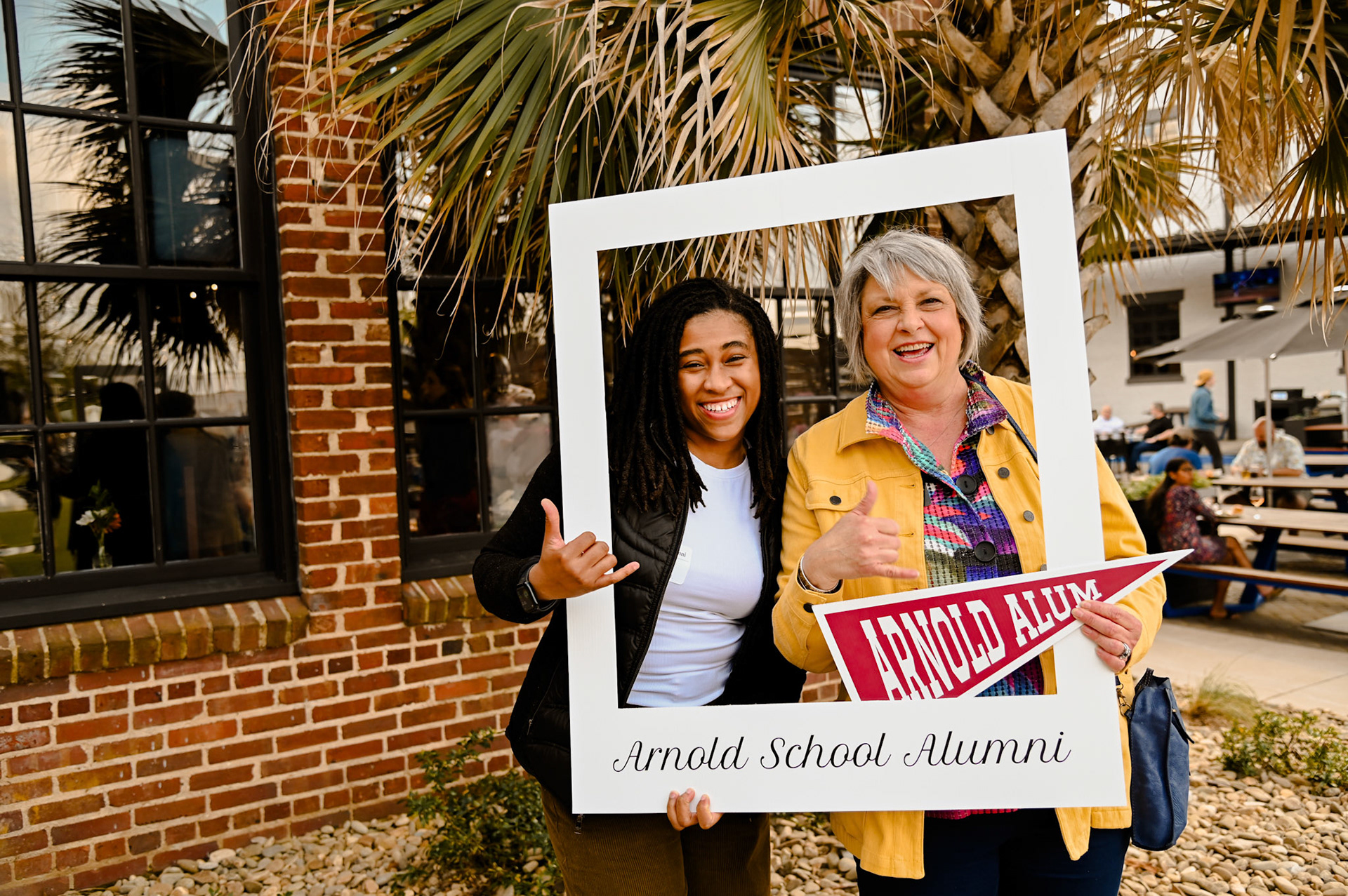 Brittany Sutton and Rebecca Jordan posing with a large photo frame that says "Arnold School Alumni"