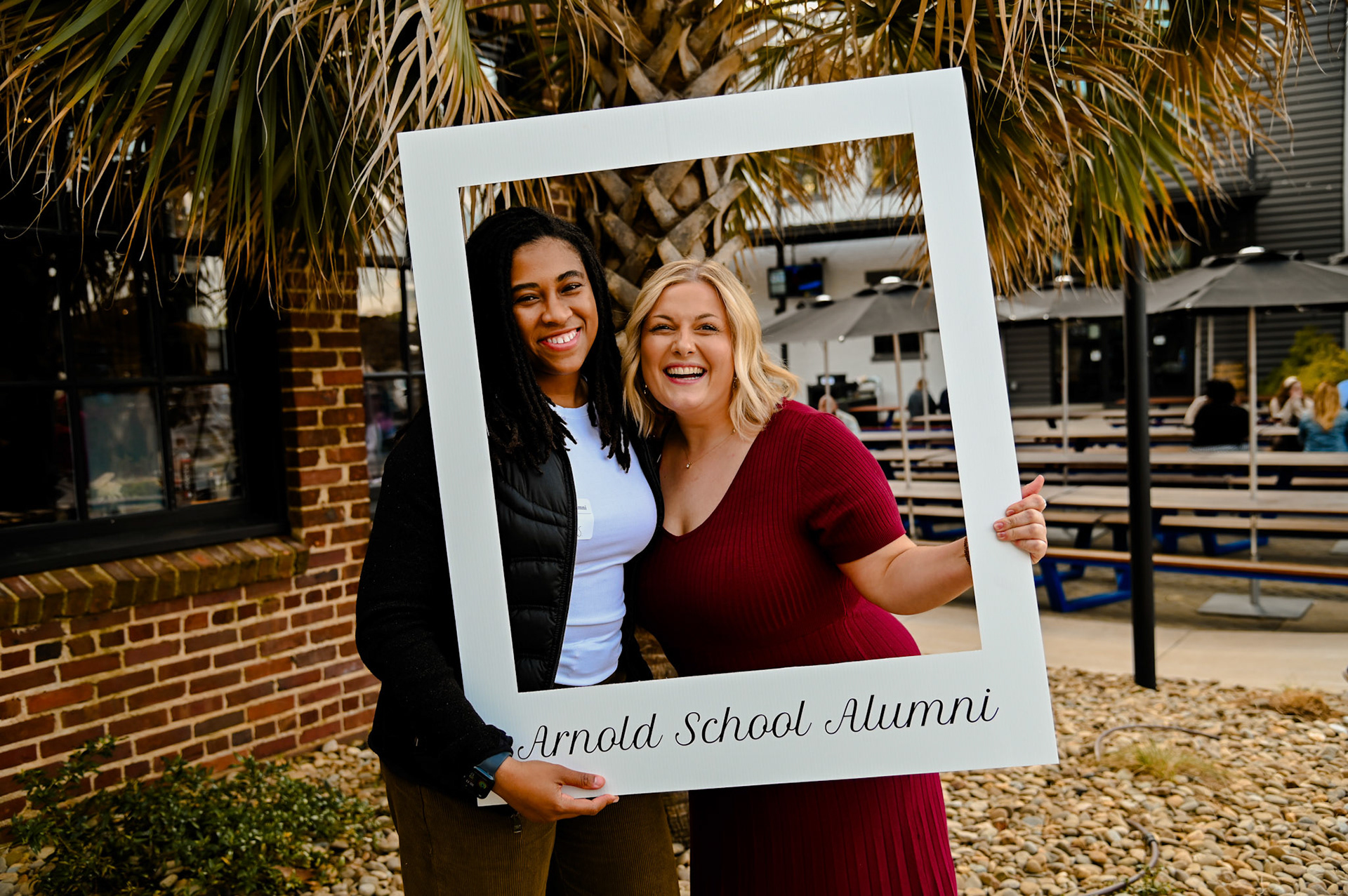 Brittany Sutton and Abigail Collins posing with a large photo frame that says "Arnold School Alumni"