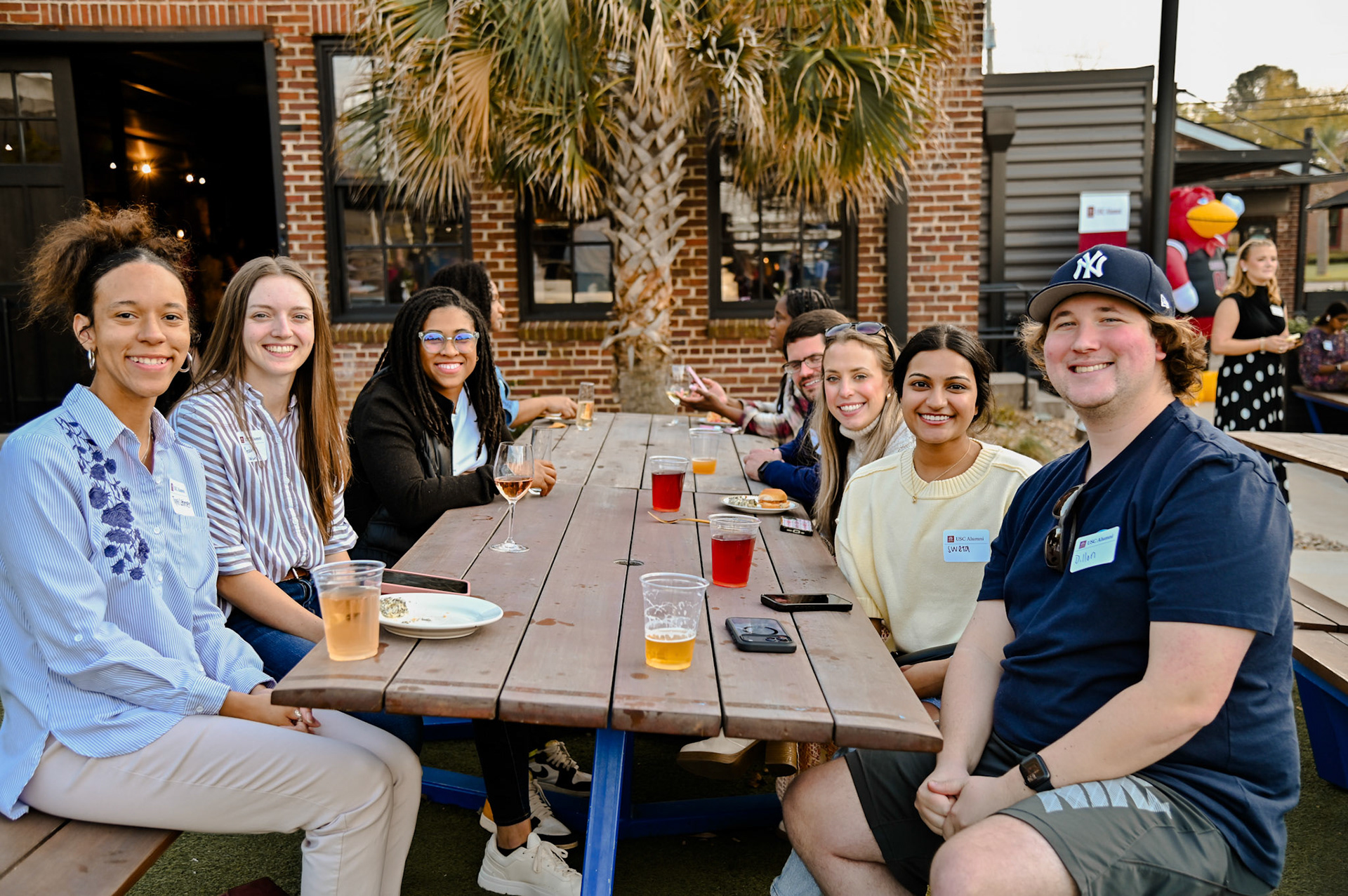 Group of alumni sitting outside at a picnic table smiling at the camera