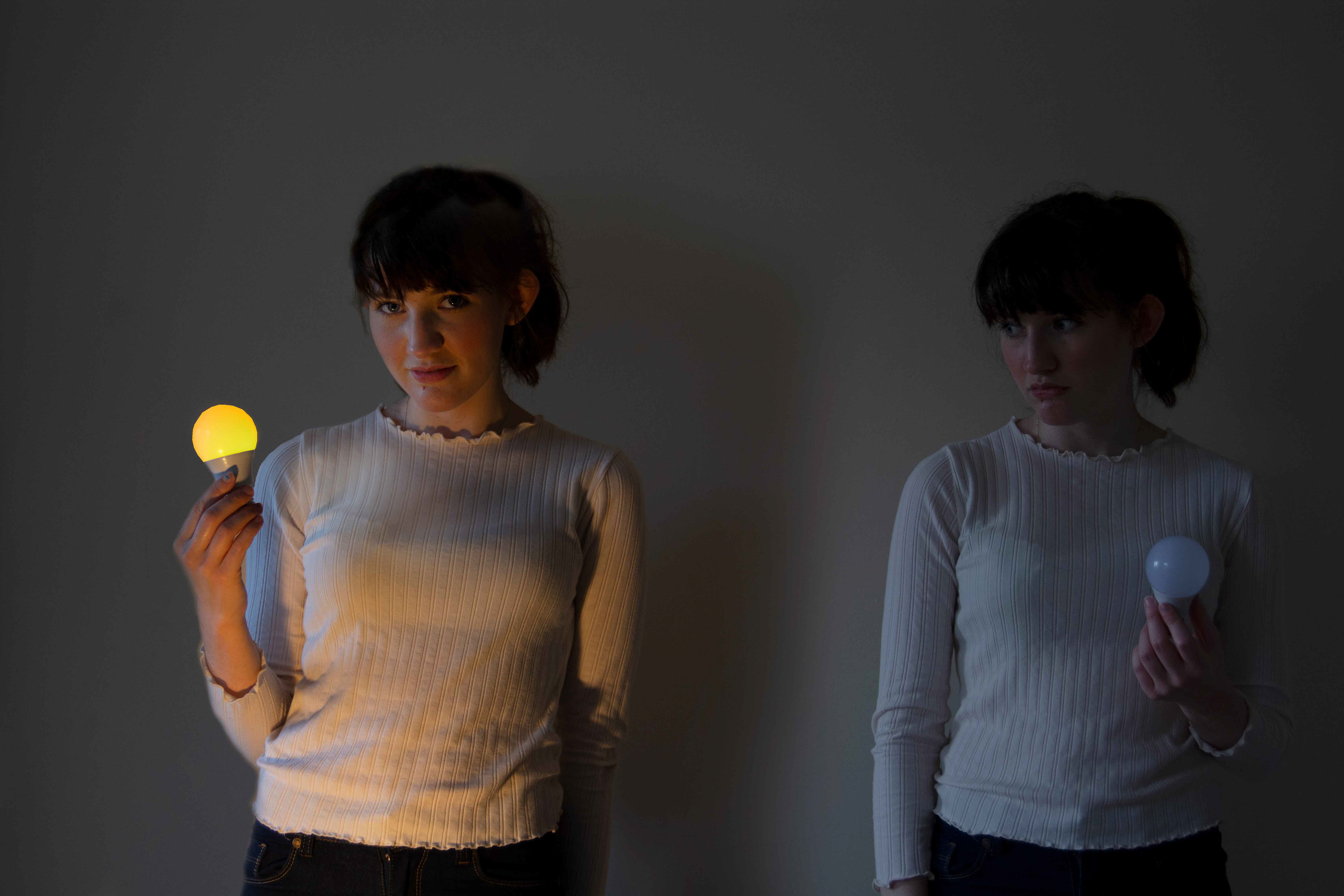 Two women hold two bulbs, one is bright, one is dim.