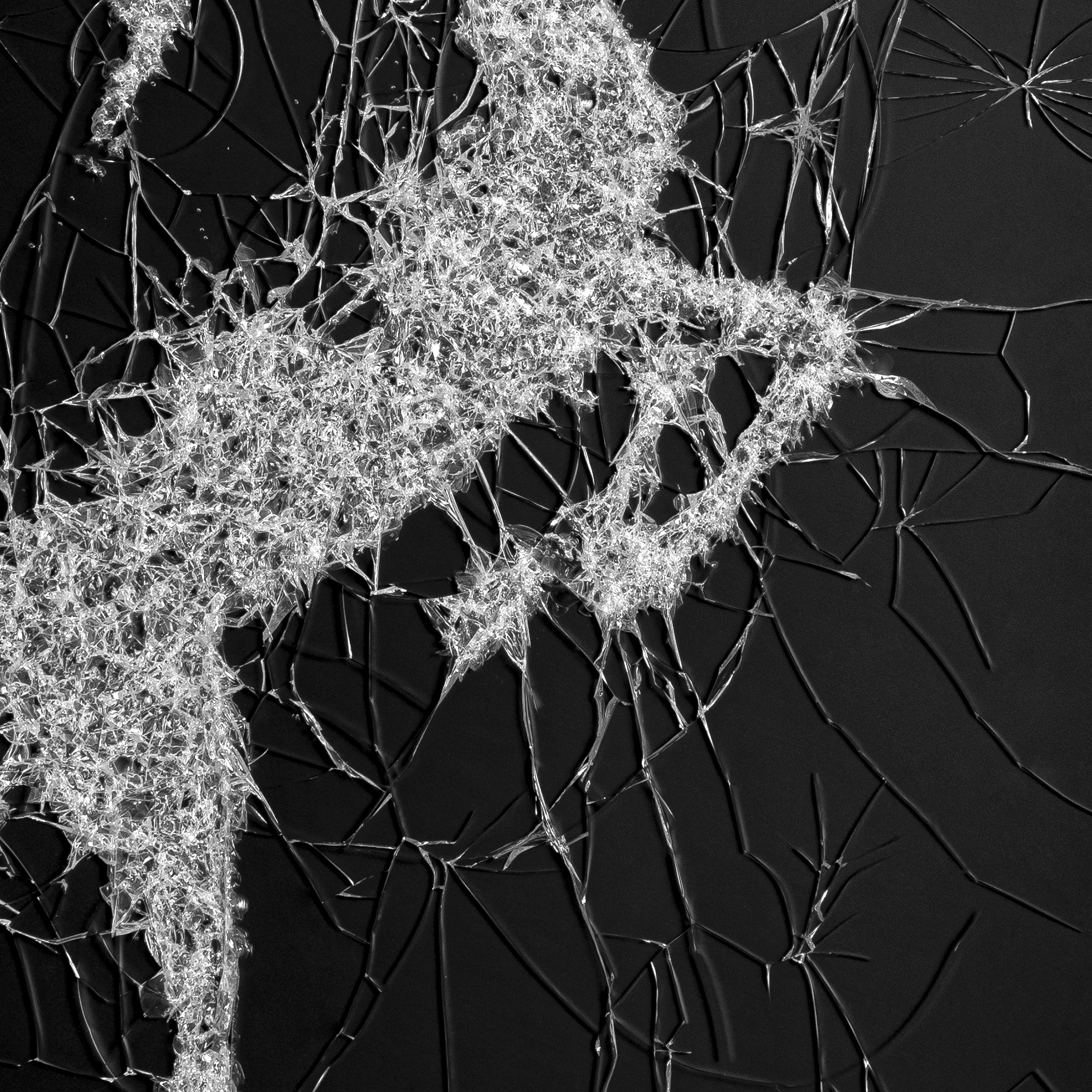 Detail van gebroken glas in een abstract patroon, met reflecties van licht en kleur.