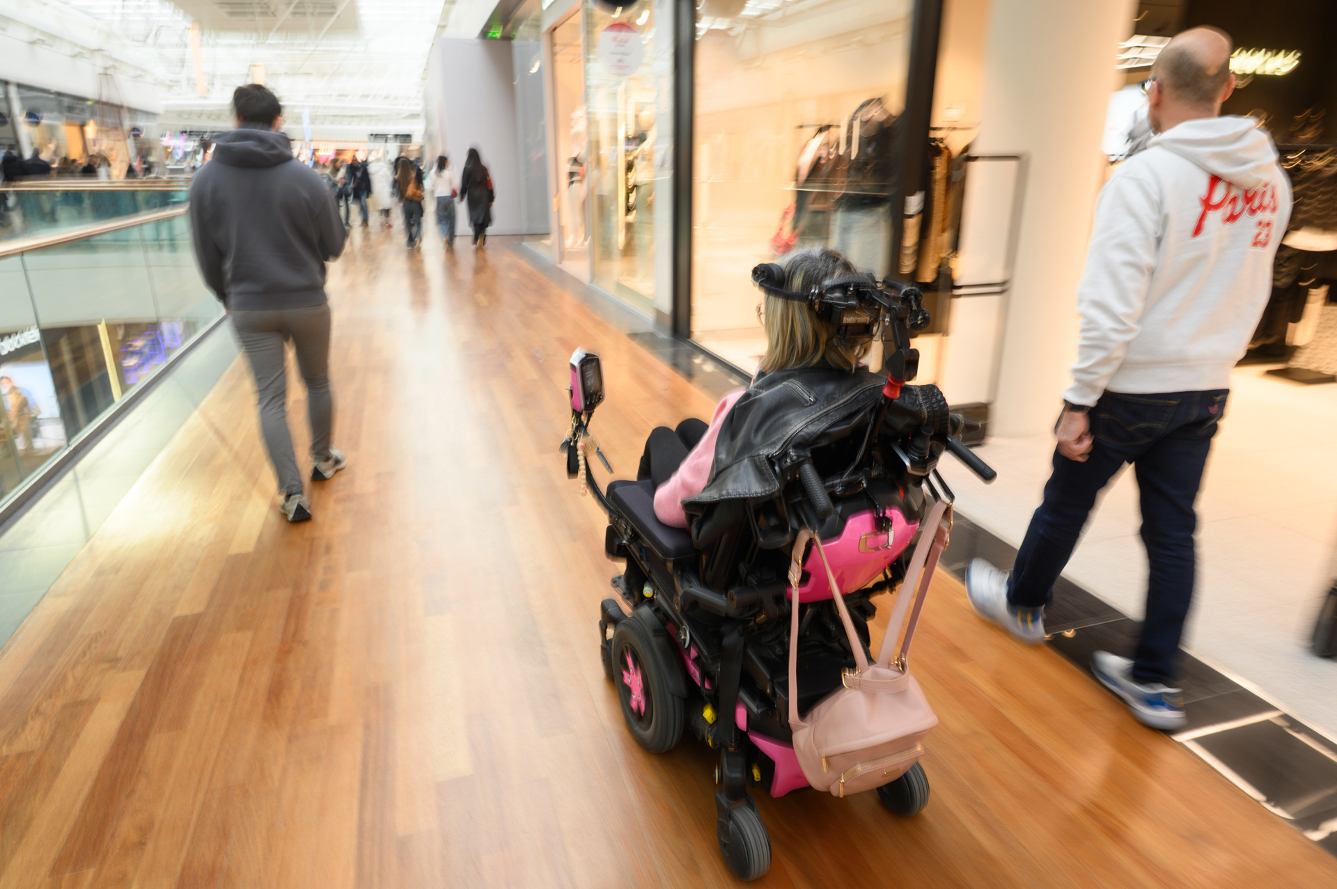 Lydie dans une des allées du centre commercial Carré Sénart, son fauteuil est rose et c’est sa couleur préférée.