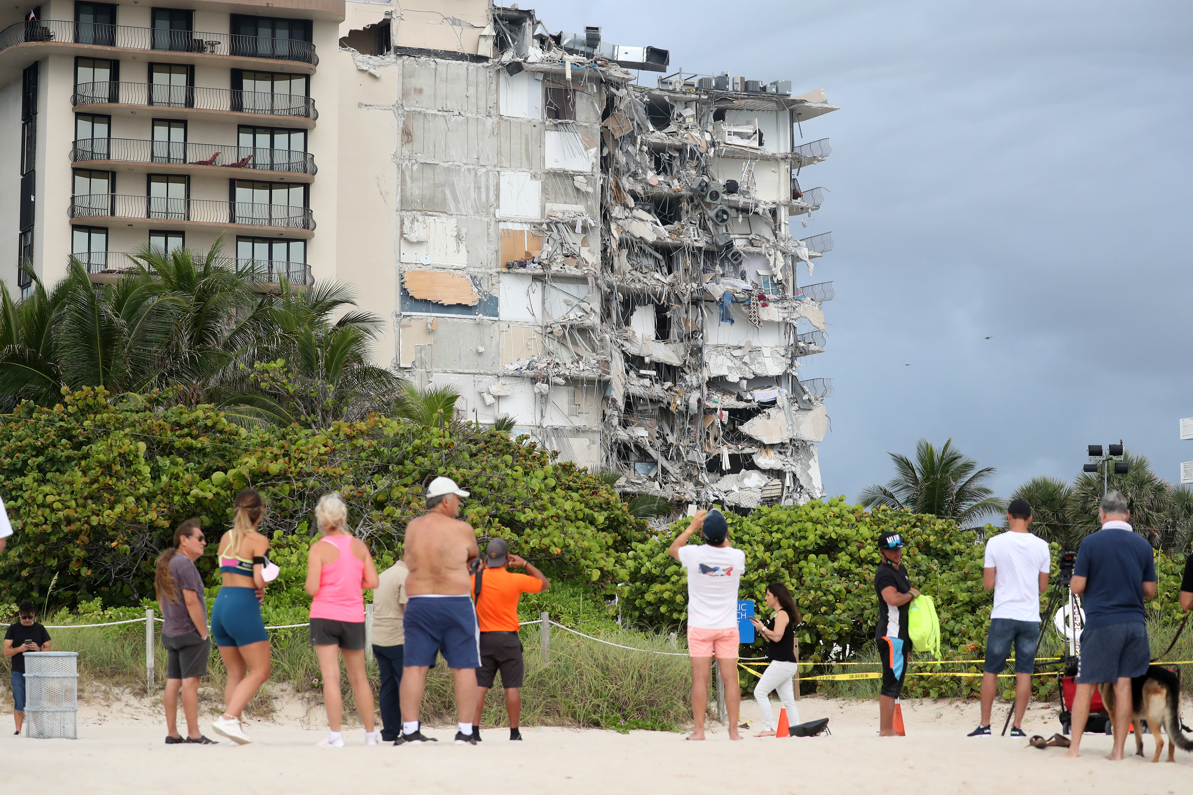 Hours after its collapse, people look at the Champlain Towers South, a 12-story beachfront condominium in Surfside, Fl. that partially collapsed, causing the deaths of 98 people.