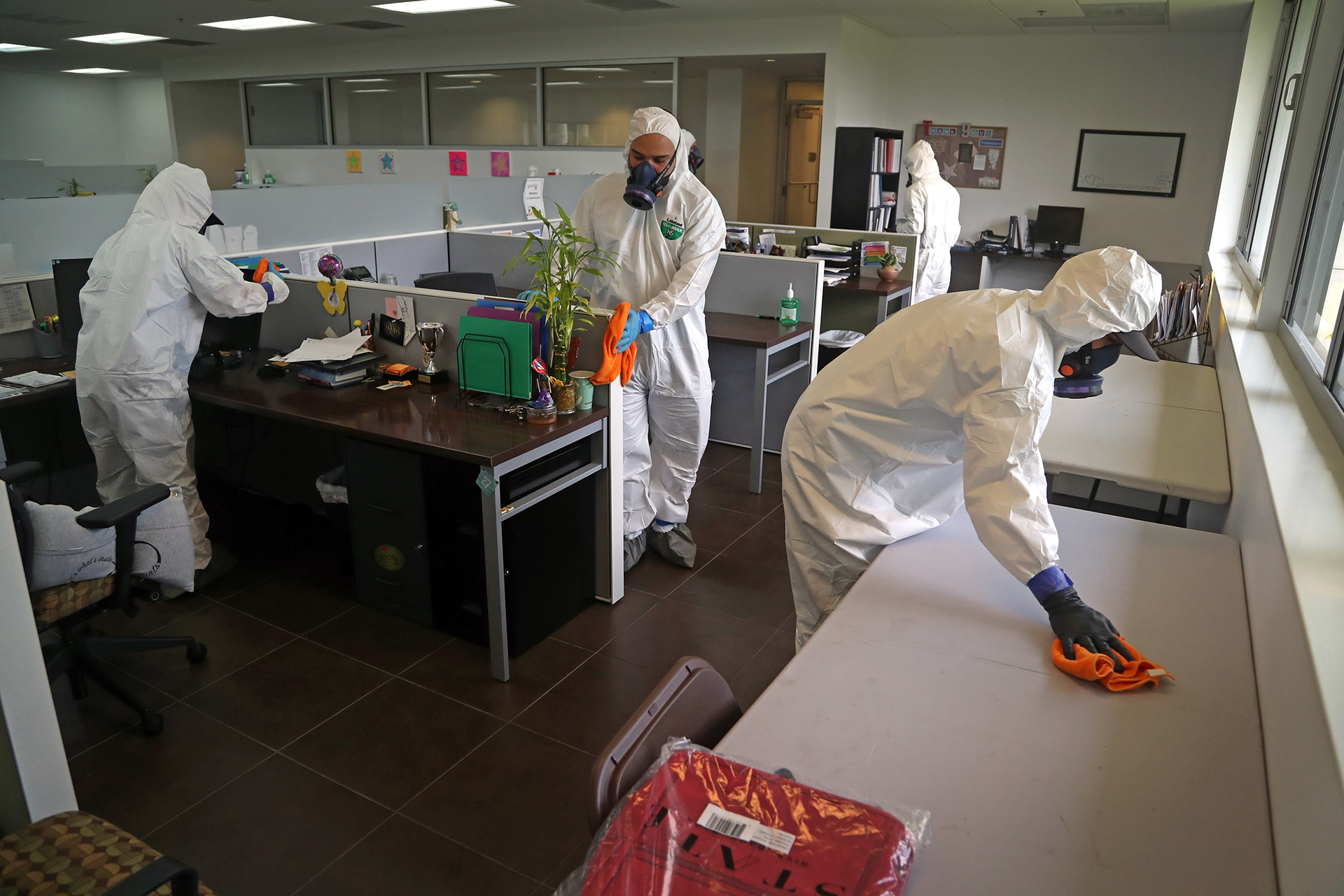 A team of technicians with a restoration company wipes down desk surfaces with disinfectant while doing a deep clean at an office building in Sunrise, Fl.. during COVID pandemic in 2020. 