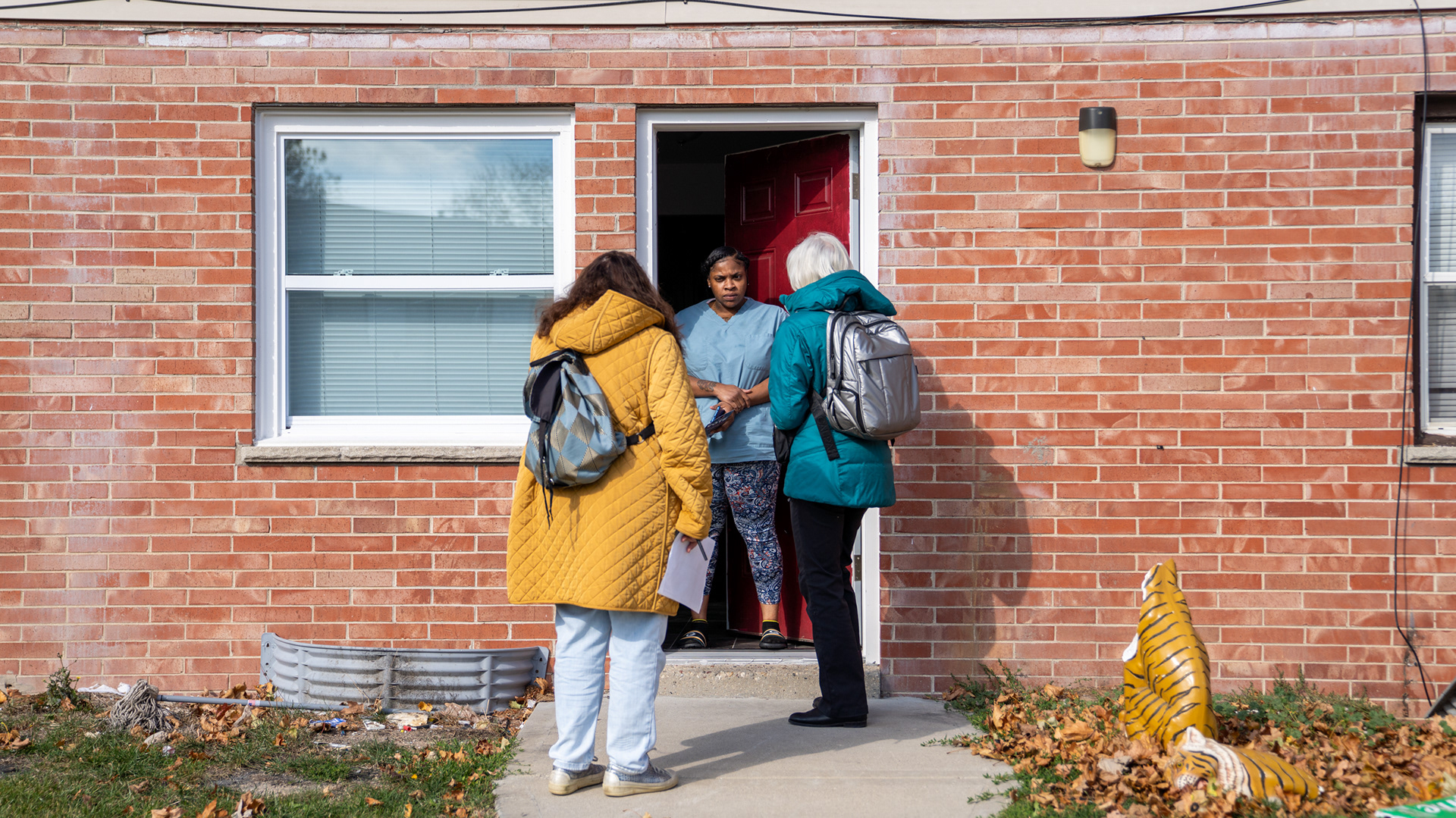 Kunda (in yellow) and Douglass (in blue) speak to a voter at her townhome in Dineen Park, a working-class, low-income neighborhood of Milwaukee. 