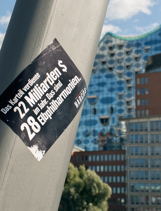 Ein kontextueller Aufkleber, der mit beeindruckenden Fakten für die Netflix Serie Narcos wirbt. Er ist in Sichtweite der Elbphilharmonie in Hamburg platziert. Auf dem Aufkleber steht: Das Kartell verdiente 22 Milliarden $ im Jahr. Das sind 28 Elbphilharmonien. Narcos. Ein Netflix Original.