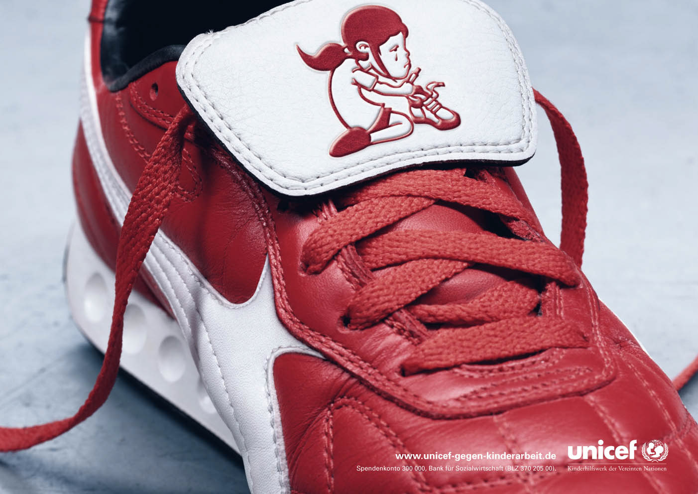 Ein Plakat, die für das Engagement von UNICEF wirbt. Wir sehen einen rot-weißen Turnschuh mit einer außergewöhnlichen Stickerei: Sie zeigt ein unglückliches Kind, das auf Knien hockt und einen Turnschuh fertigen muss. Darunter steht: www.unicef-gegen-kinderarbeit.de. Dazu das Spendenkonto und das Logo von Unicef.