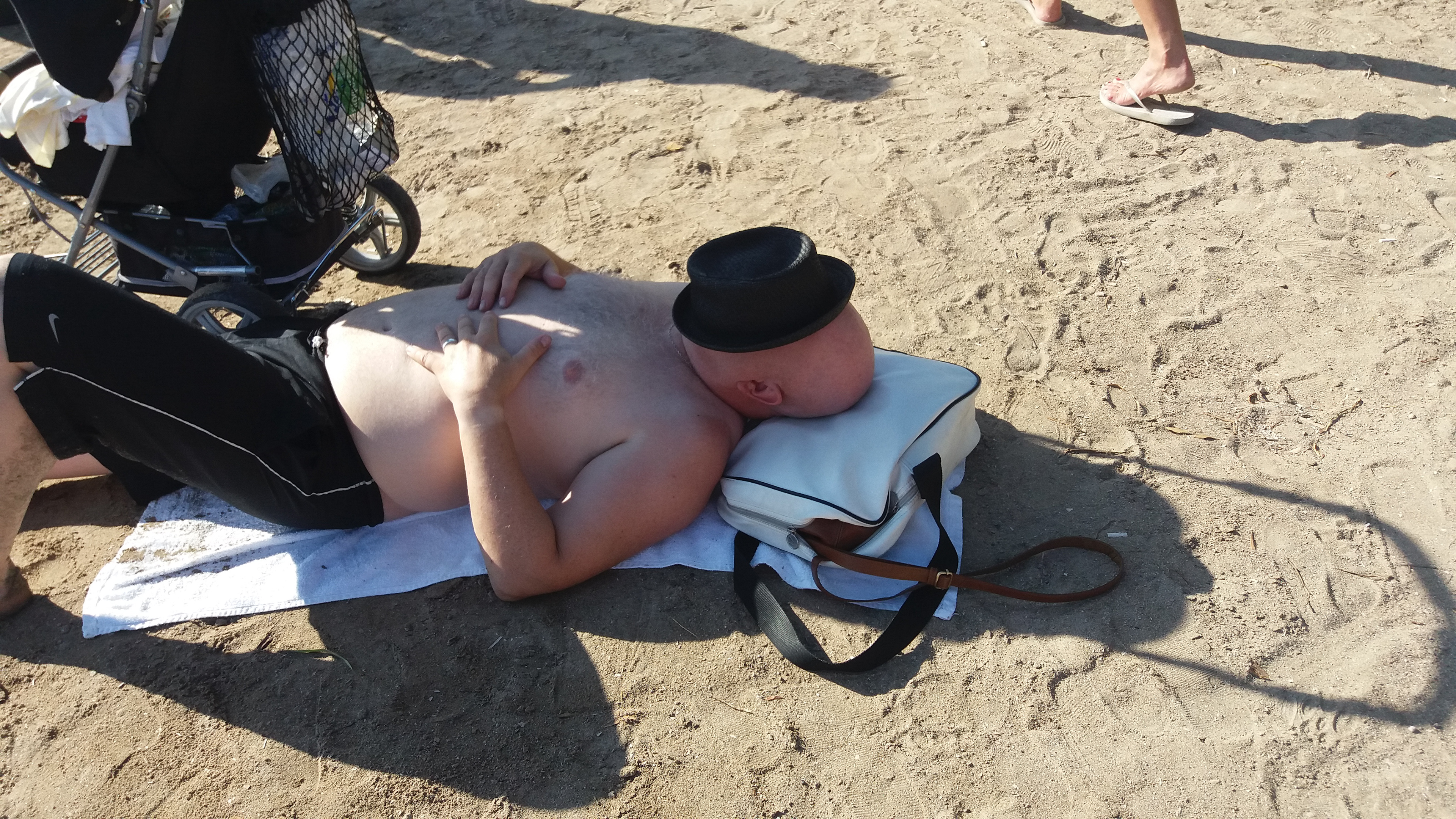 Relaxing in style! A man on the sand uses a bag as a pillow, while his hat adds a unique touch.Χαλάρωση με στυλ! Ένας άνδρας στην άμμο χρησιμοποιεί μια τσάντα ως μαξιλάρι, ενώ το καπέλο του δίνει μια μοναδική πινελιά.