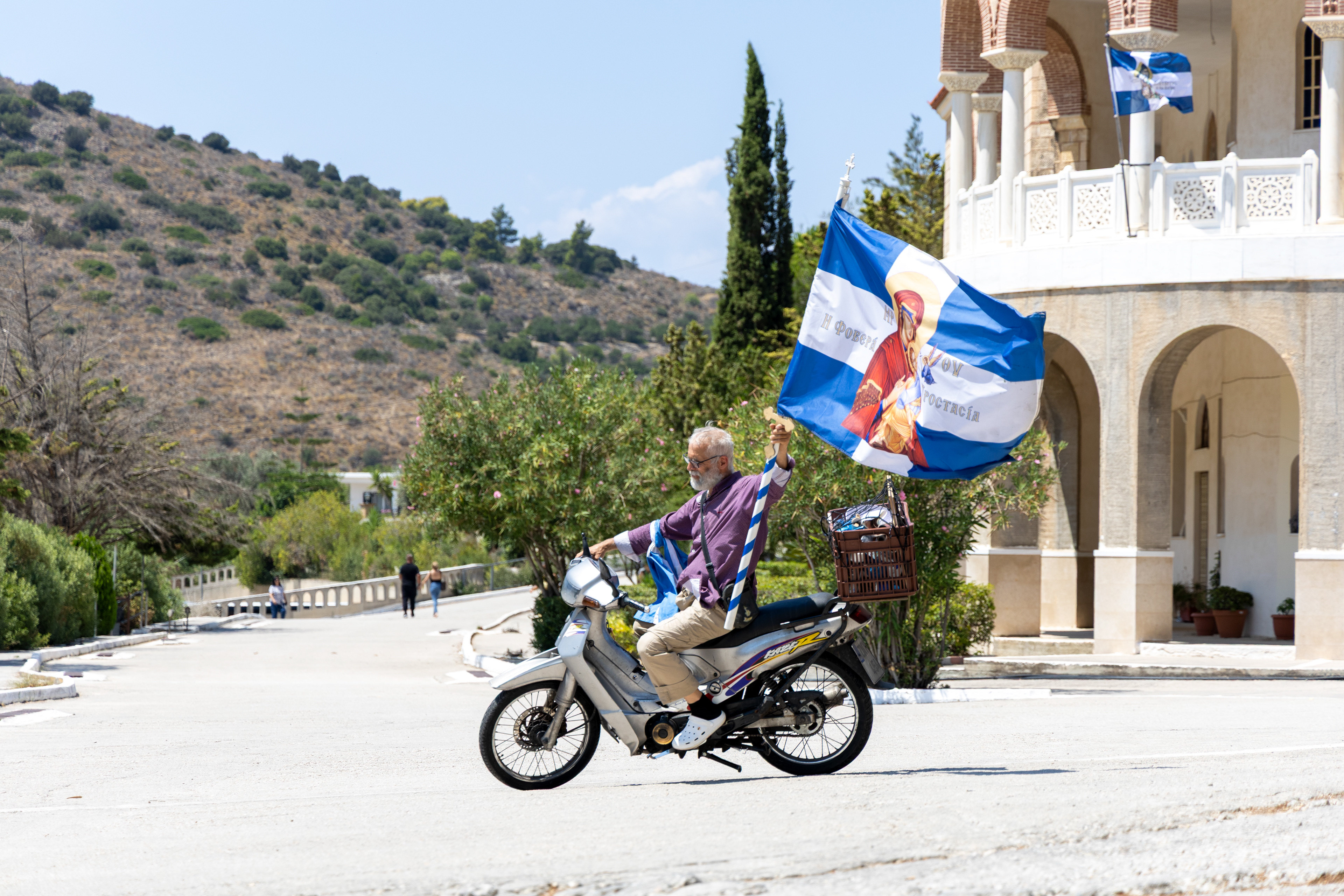 Man riding a motorbike carrying a large religious flag outside the Monastery of Saint Nektarios in Aegina, Greece.