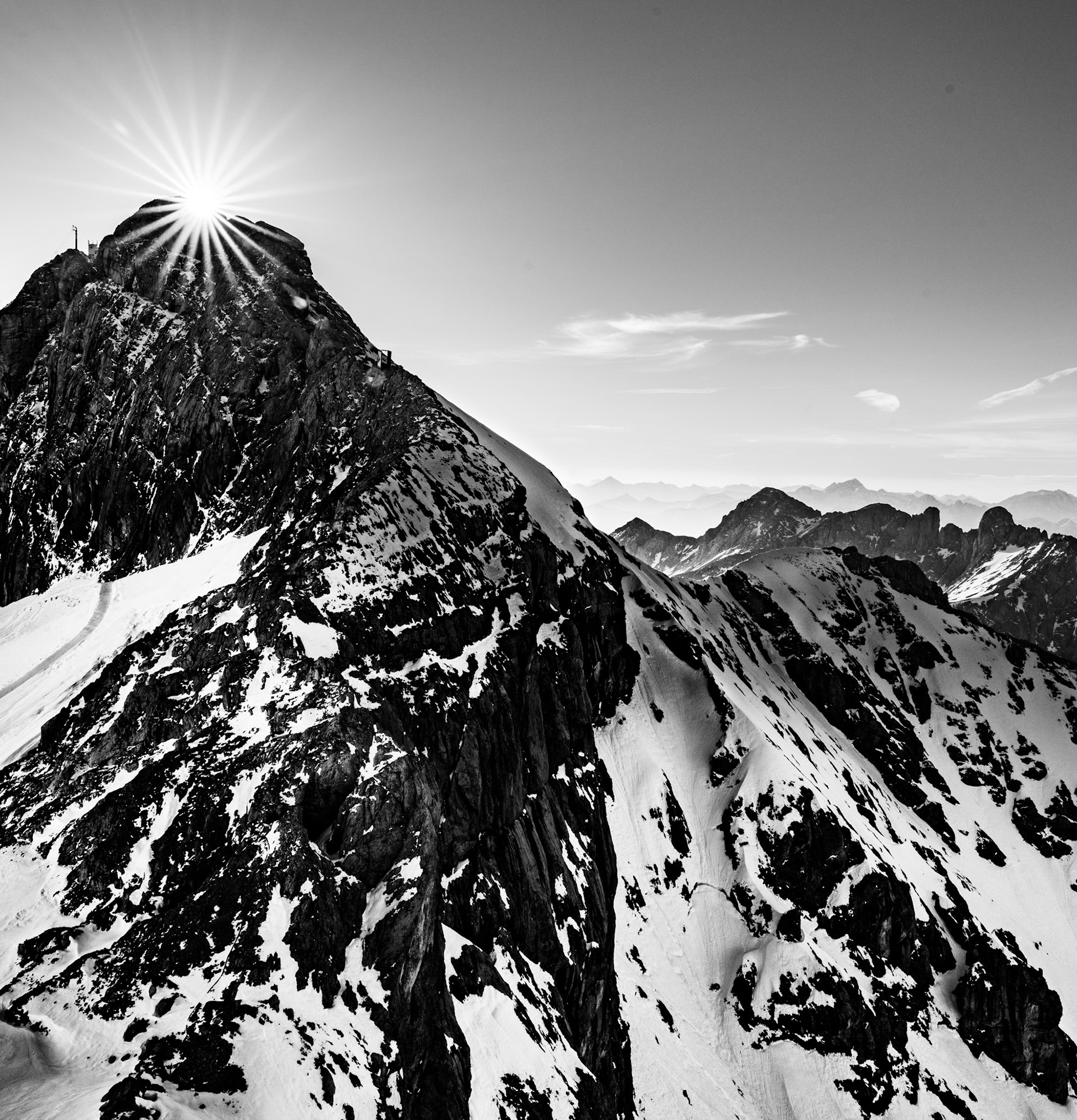 Layers of distant mountains visible in this Austrian alpine scene, with a sun star. Black and White