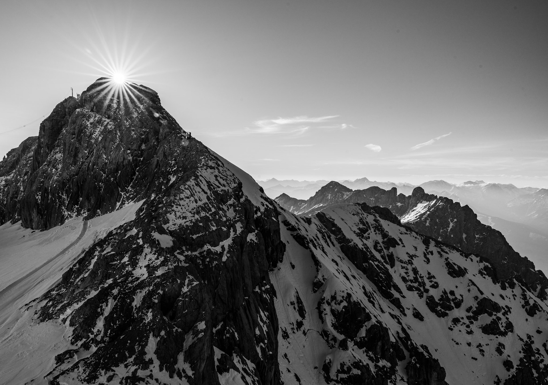 Layers of distant mountains visible in this Austrian alpine scene, with a sun star. Black and White
