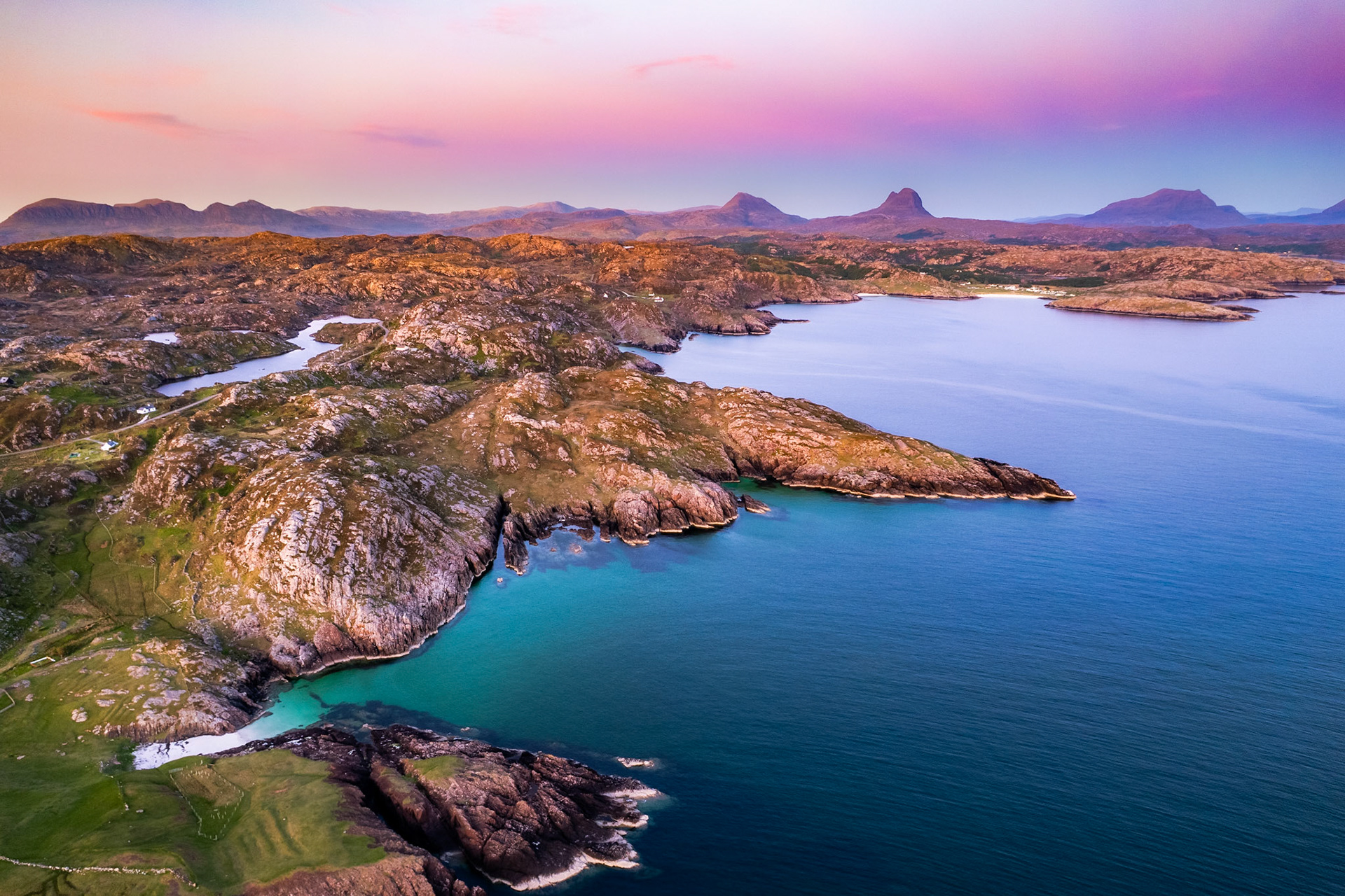 The gneiss rock, billions of years old, meets the turqoise waters of the Atlantic on the West coast of Scotland. Distant mountains sit on the horizon, looking absolutely majestic.