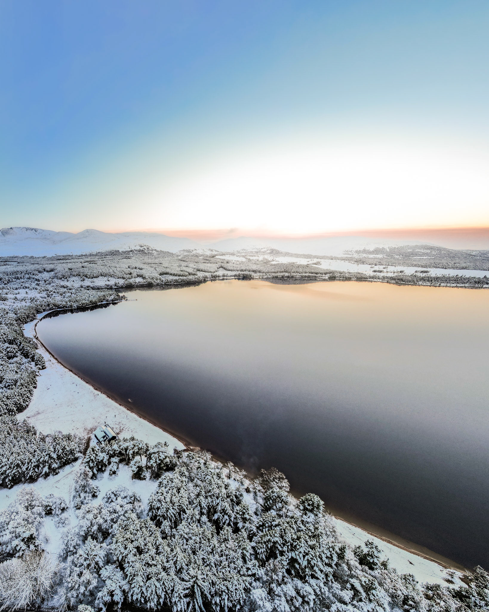 A winter Loch Morlich, with a clear sky, the water still and the forest covered in white snow. Cairngorms, Scotland