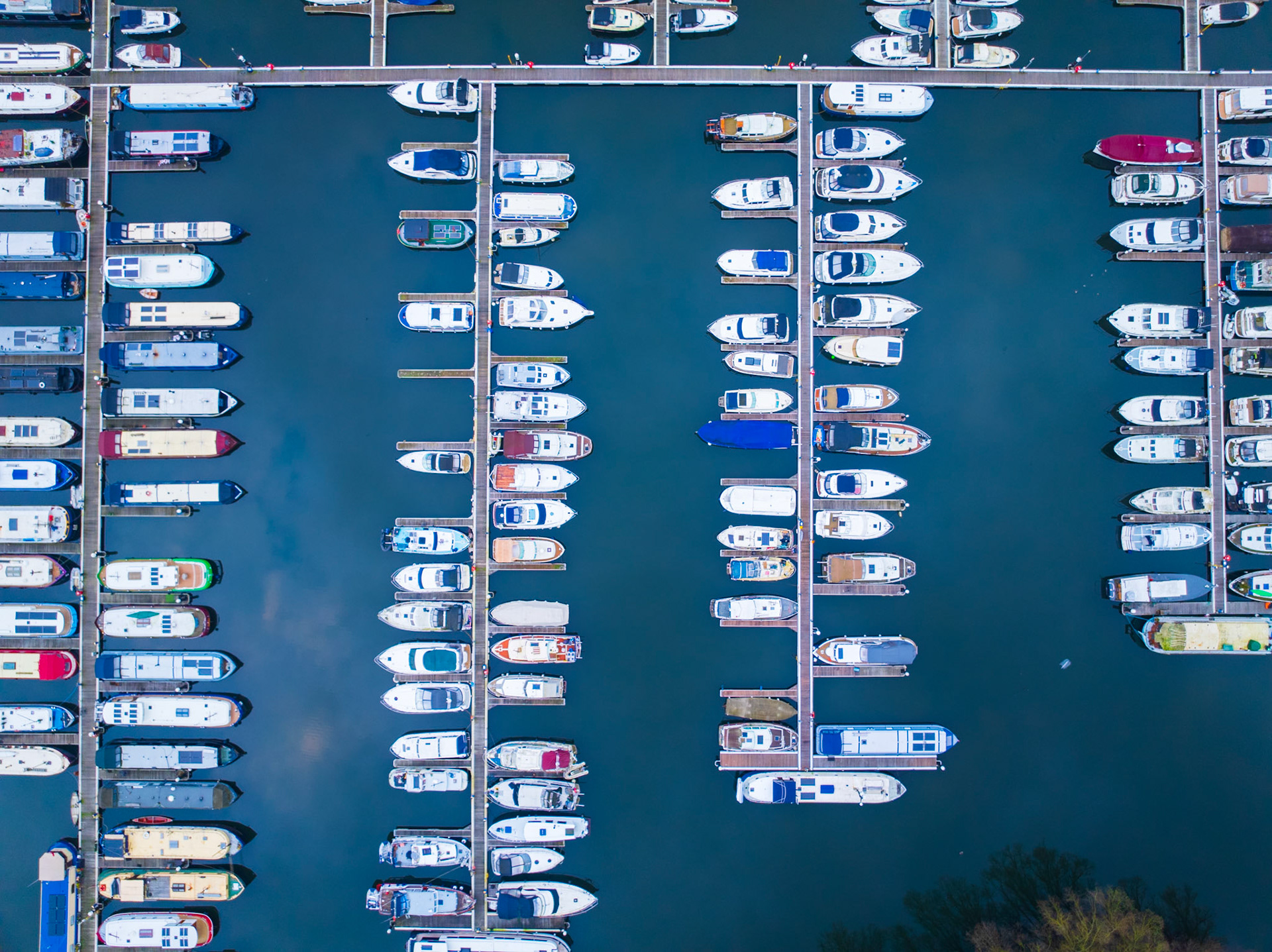 Dozens of leisure craft moored in parallel pontoon lanes at a marina near Reading, photographed from directly overhead in flat winter light. The geometric regularity of hulls and walkways dominates, with dark still water filling the intervals between vessels.