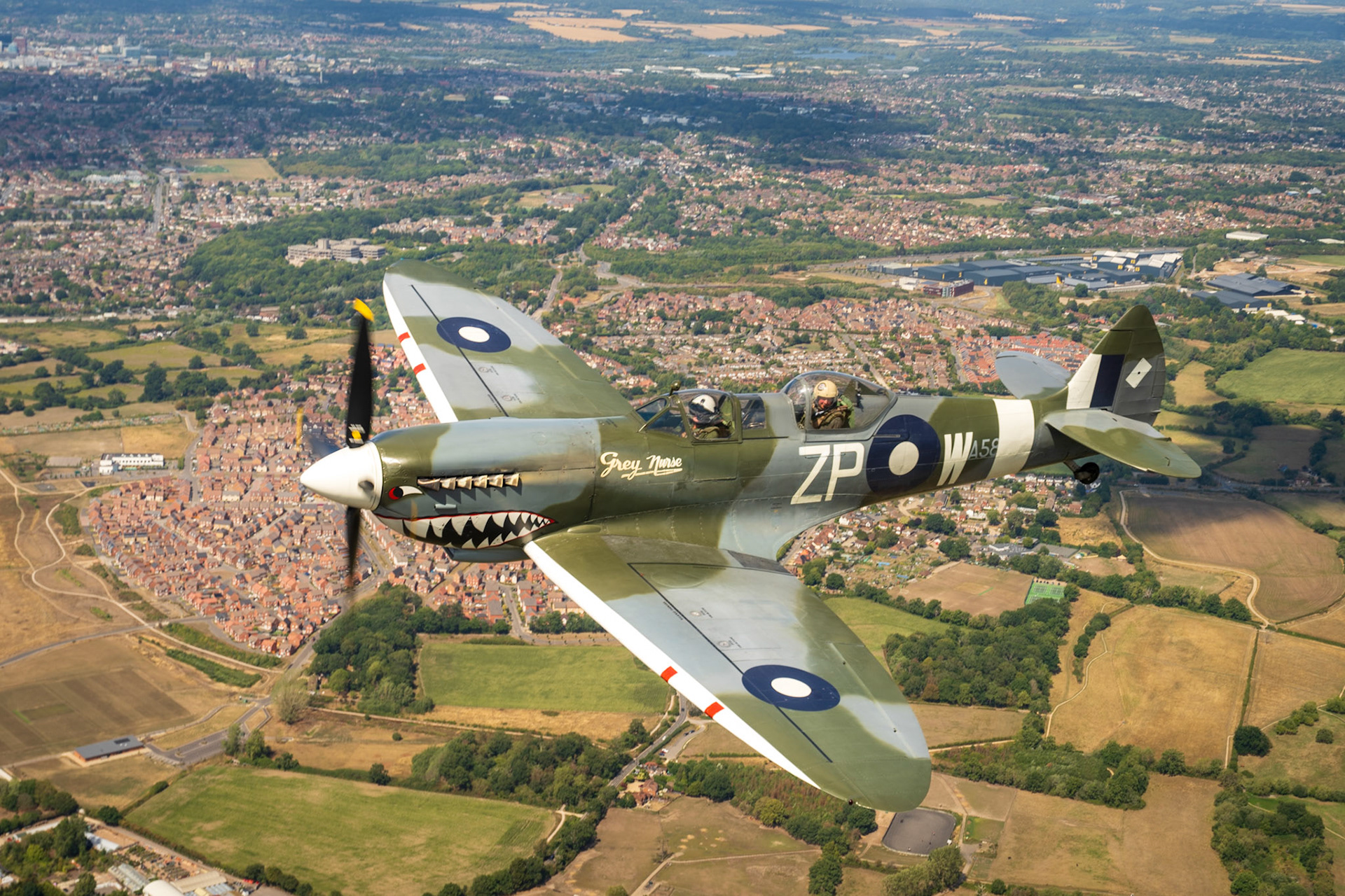 Spitfire in flight over british countryside and town.
