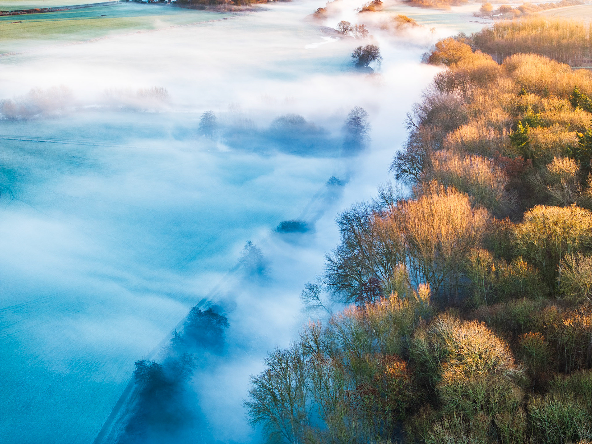 An image captured on a frosty misty morning in Oxfordshire - where warm sunrise light hits trees and the mist sits below on the River Thames and neighbouring fields. A real demonstration of the DJI Mavic 3 Pro dynamic range and colours.