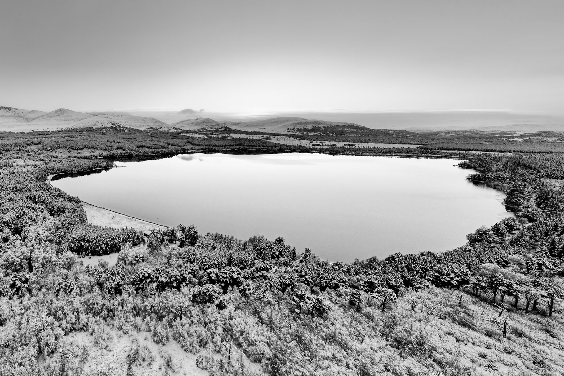 A winter Loch Morlich, with a clear sky, the water still and the forest covered in white snow. Cairngorms, Scotland