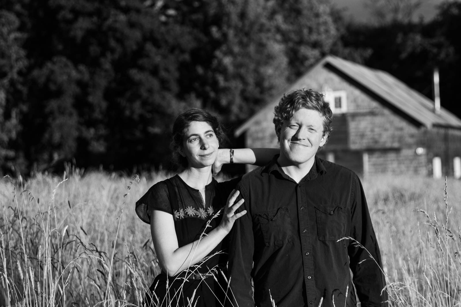Couple stands in field of tall grass in front of rustic barn