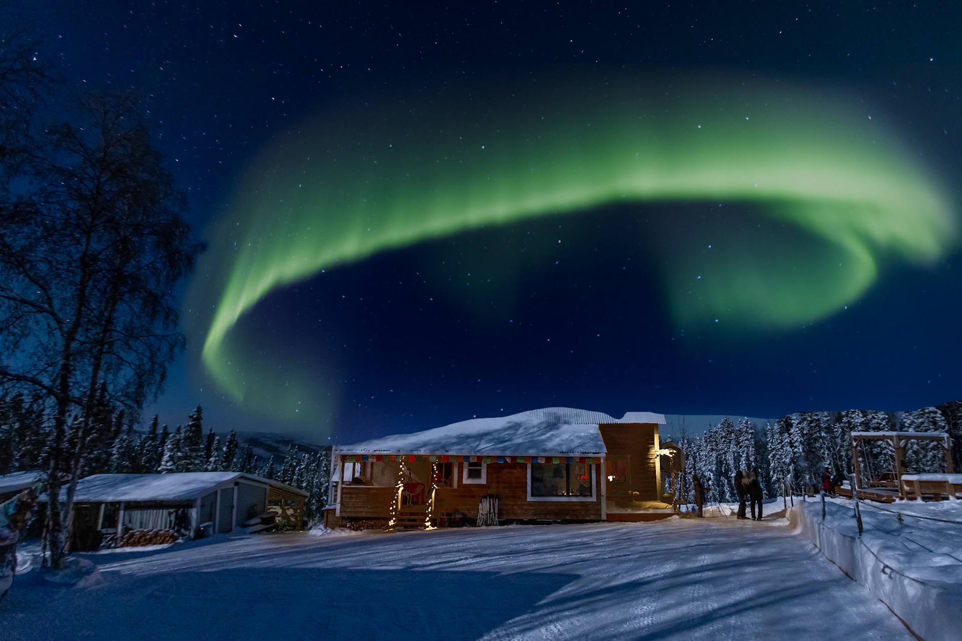 Aurora borealis almost forms a halo above lodge in northern Alaska