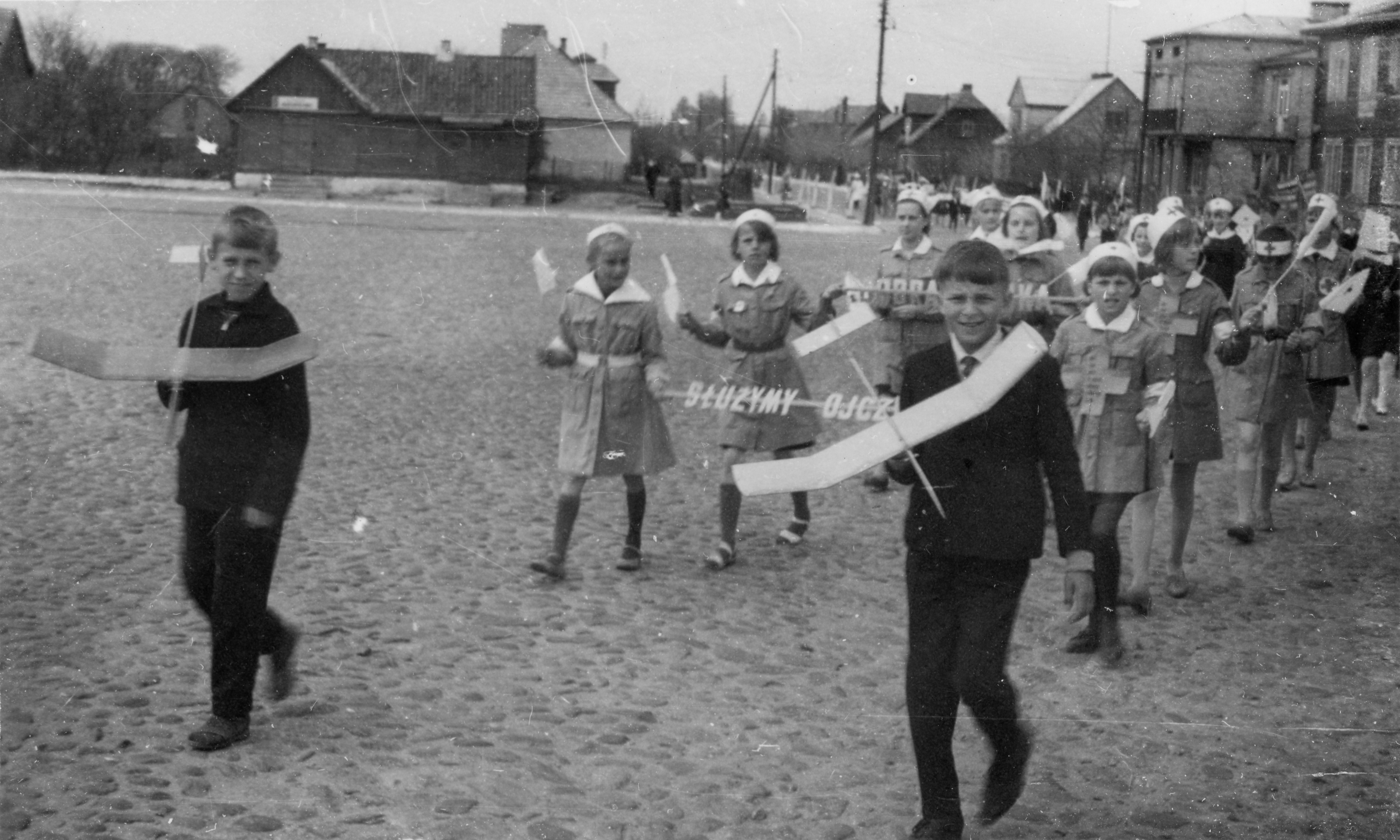 1965.05.16 | Dni Oświaty, Książki i Prasy - kółko modelarskie i harcerki maszerują ul. Rynek w Zabłudowie | z arch. Zespołu Szkolno-Przedszkolnego w Zabłudowie