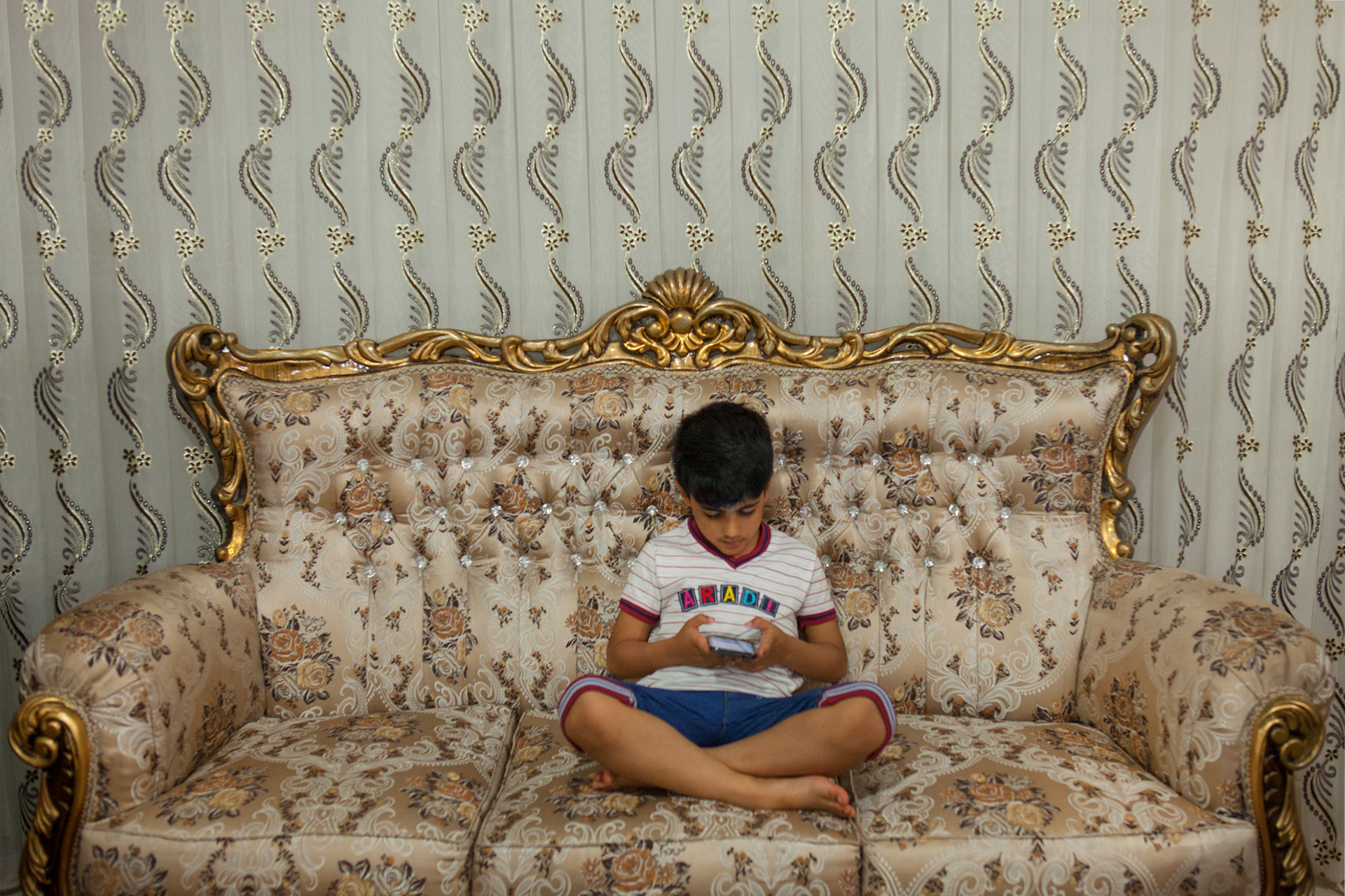 bambino iraniano che gioca ai videogiochi sul sul divano di casa sua, iran. Kid playing videogames in his house, Kashan, Iran