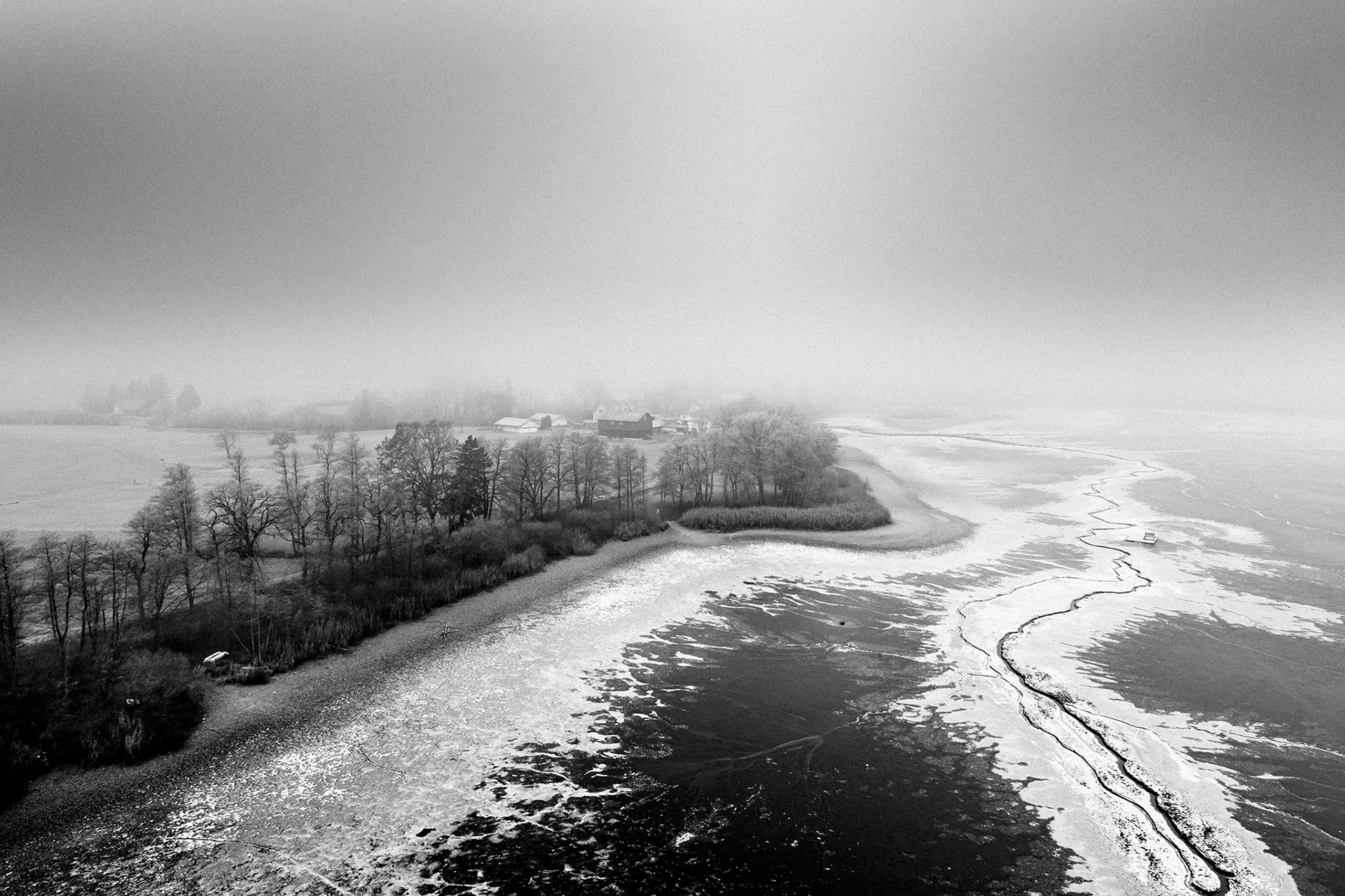 Minimalistische Schwarzweiß-Fotografie aus der Serie IM NEBEL – nebelverhangene Seelandschaft mit Baumsilhouetten im diffusen Morgenlicht von Stefan Kuhn