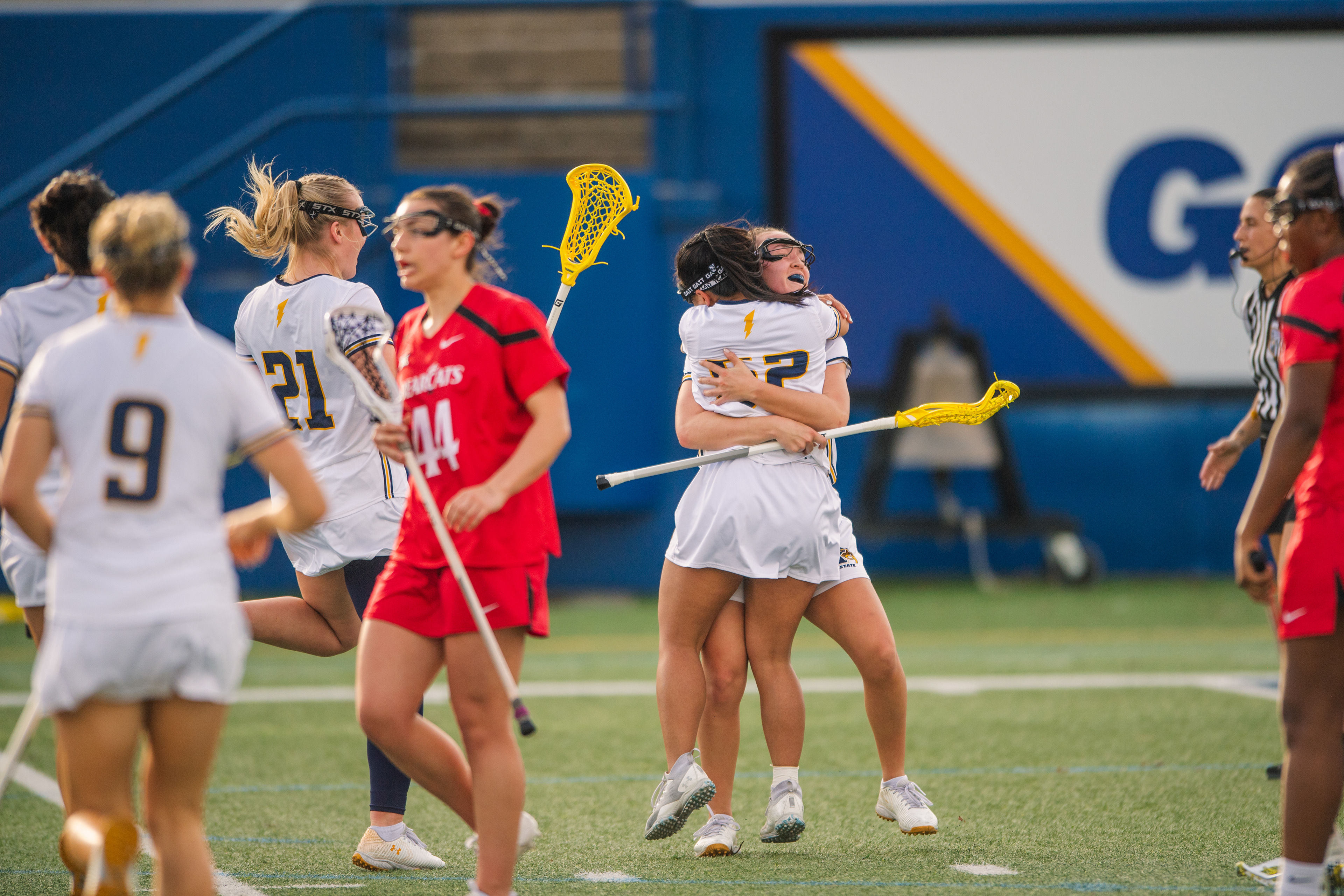 The goal lands as two Kent State attackers collide in celebration as a Cincinnati defender walks away and the afternoon light catches the moment perfectly on the home turf.