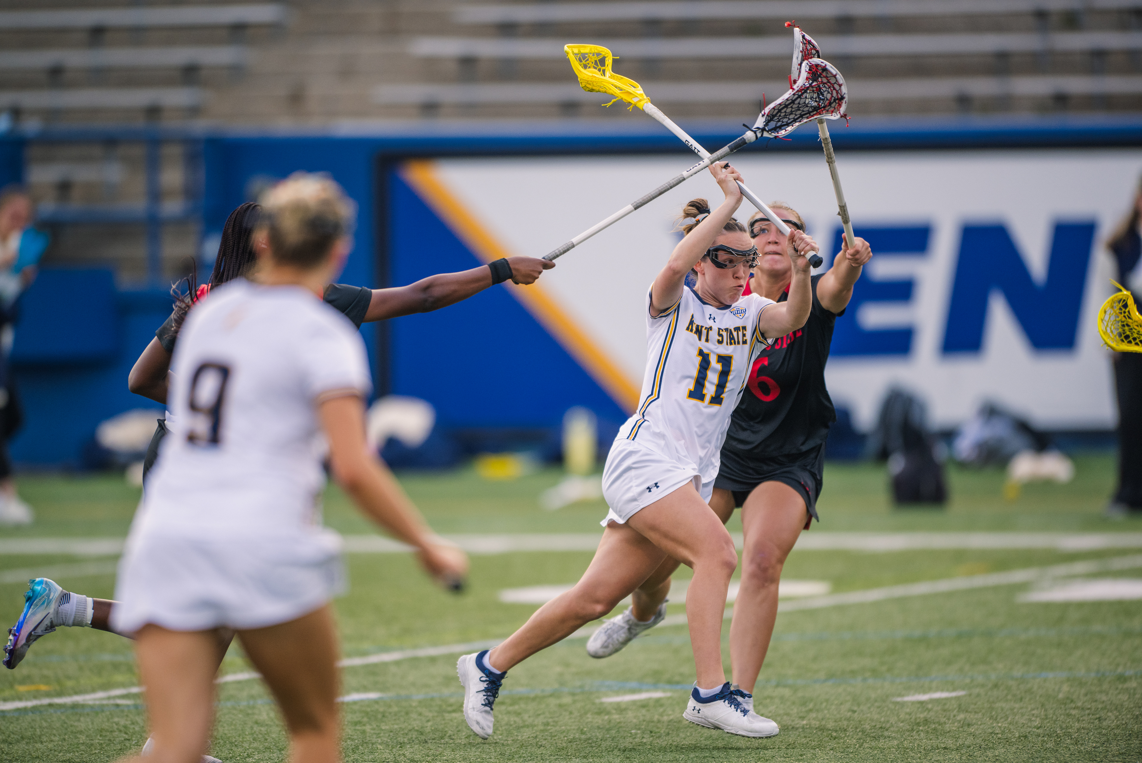 Kent State's #11 cuts through traffic against Cincinnati, absorbing pressure from two Bearcat defenders while keeping her eyes locked on the cage.