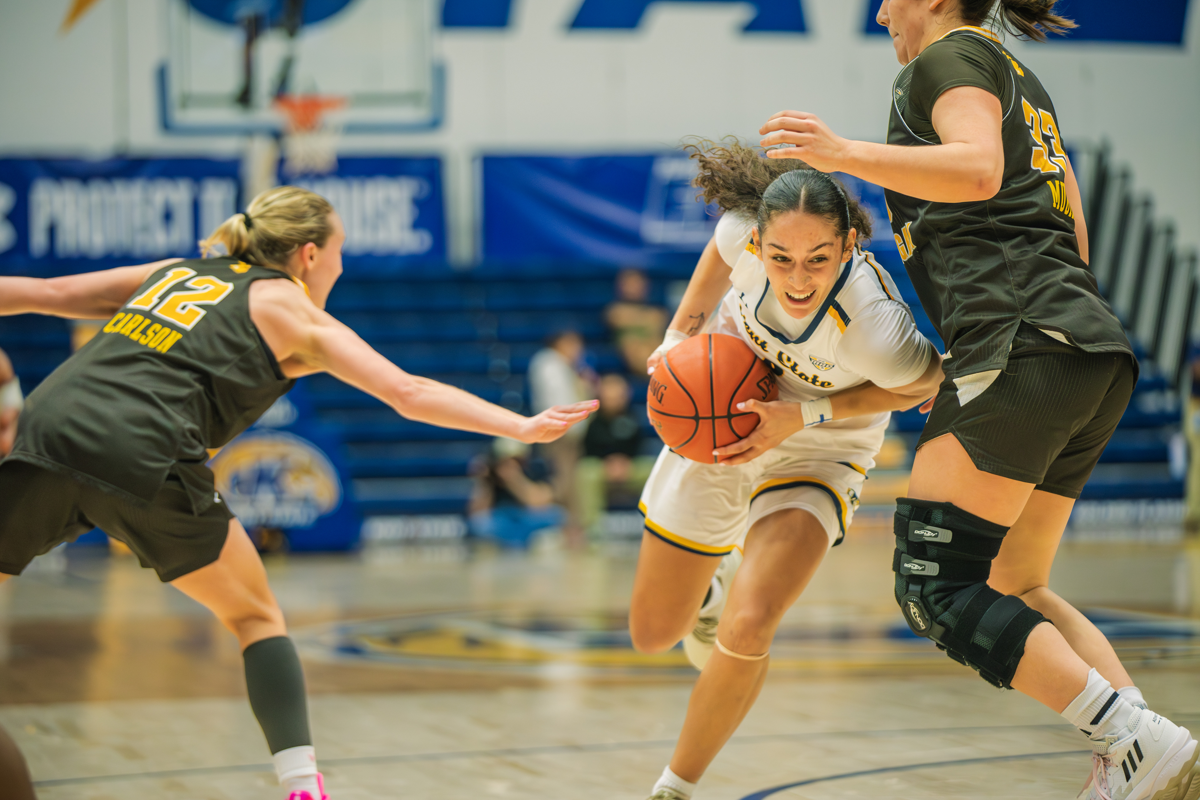 A Kent State guard splits two Western Michigan defenders on a drive to the lane, her expression locked in during a home victory over the Broncos.