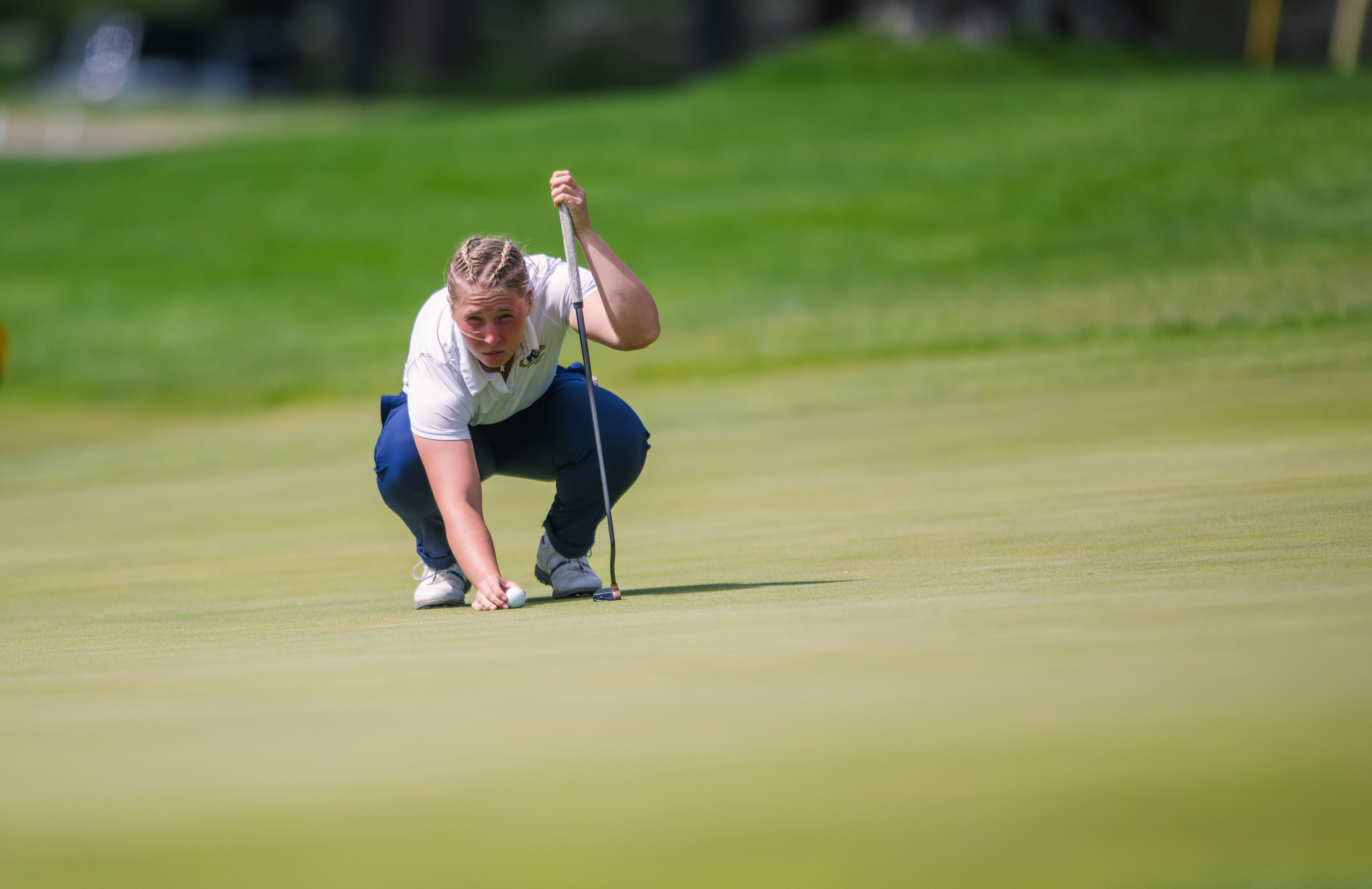 Every inch matters | A Kent State golfer reads the break on a critical putt, the afternoon sun casting long shadows across the green during the MAC Championship.