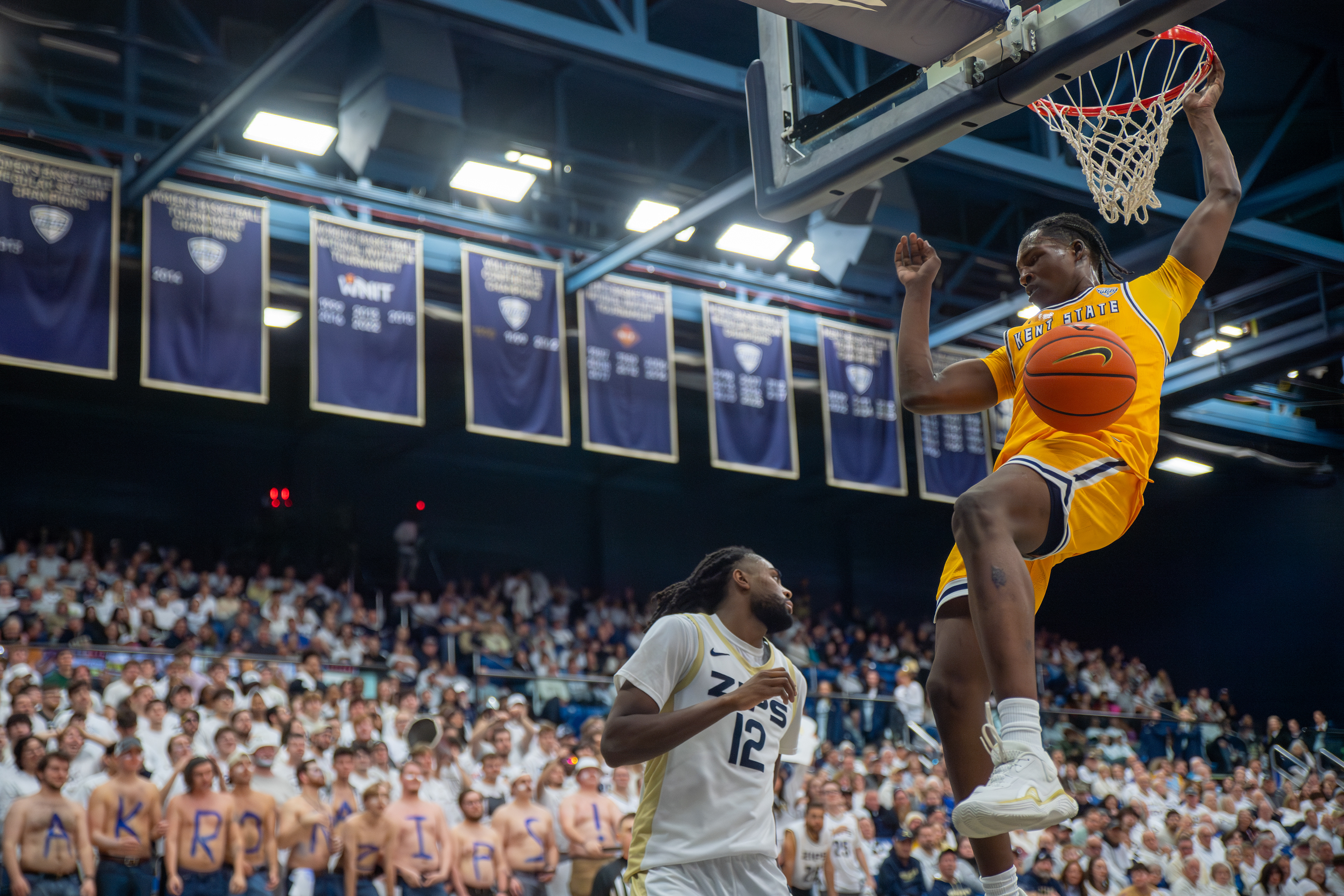 A Kent State forward throws down a two-handed dunk in front of the Akron faithful, championship banners bearing witness overhead as the Flashes silence the Zips' arena.