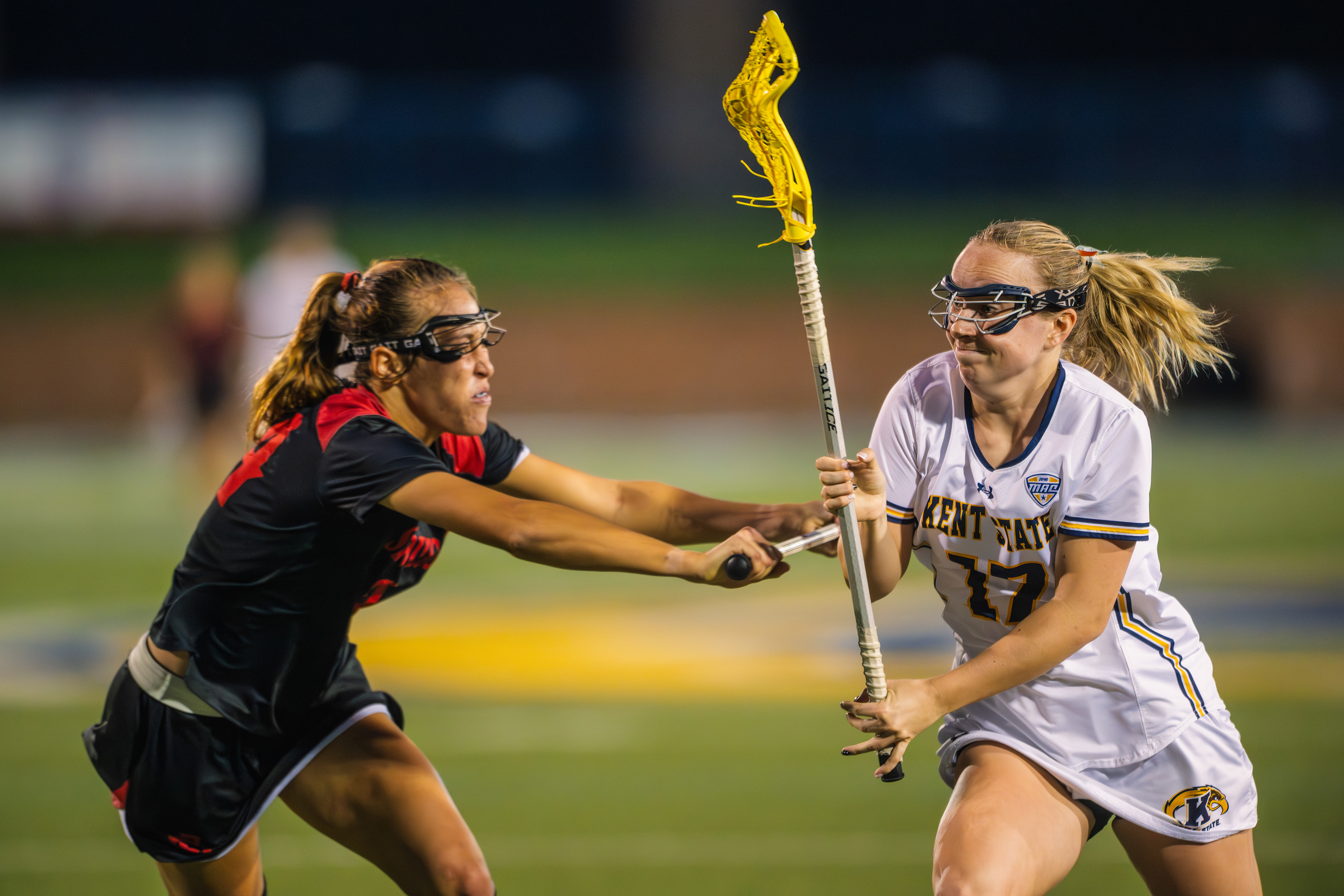 Kent State's #17 shields possession as an SDSU defender reaches across to strip the ball. Two players locked in a battle for control under the lights at Dix Stadium.