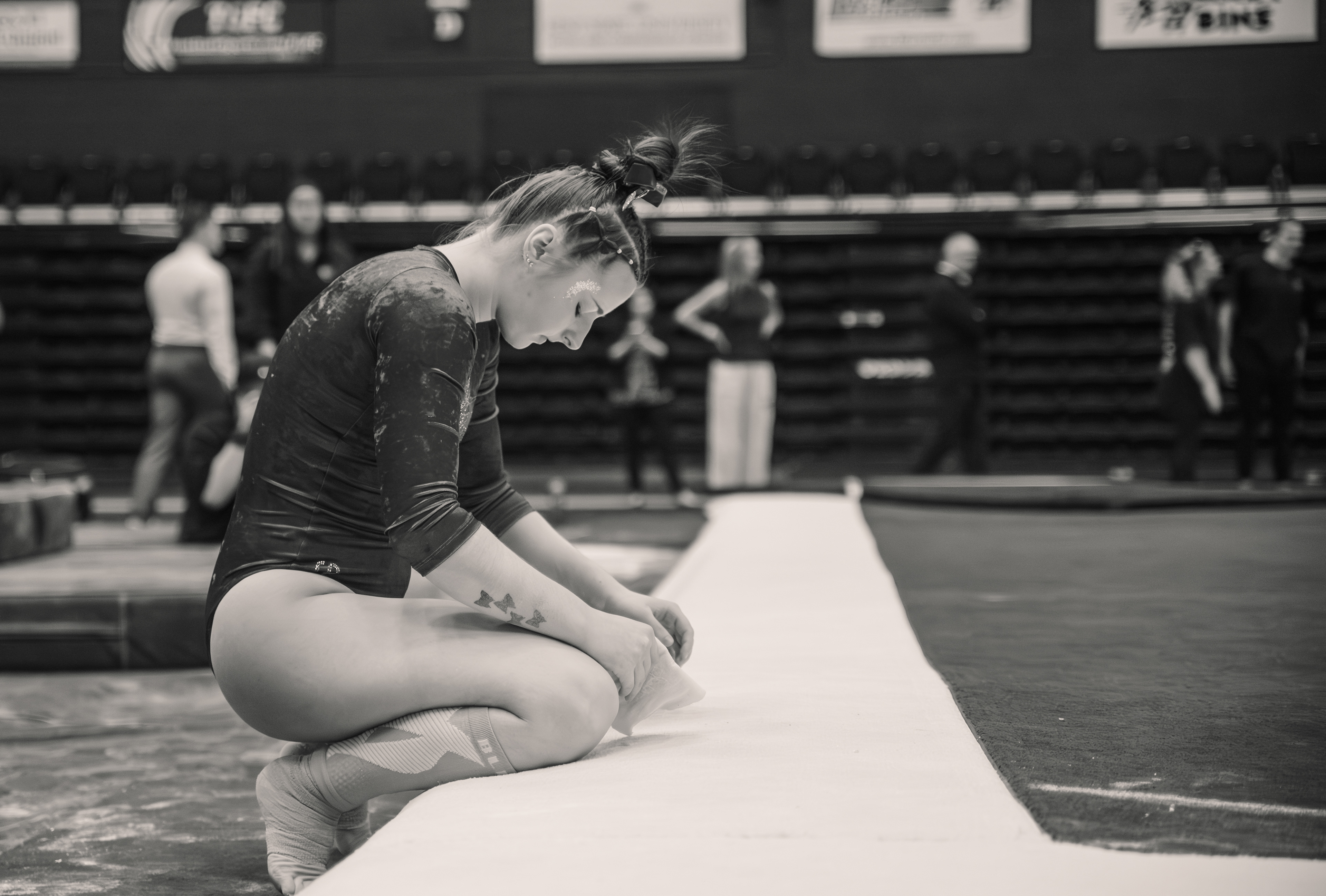 Between rotations, a chalk-dusted Kent State gymnast sits at the edge of the mat. Alone with the preparation for a moment before the competition resumes around her.