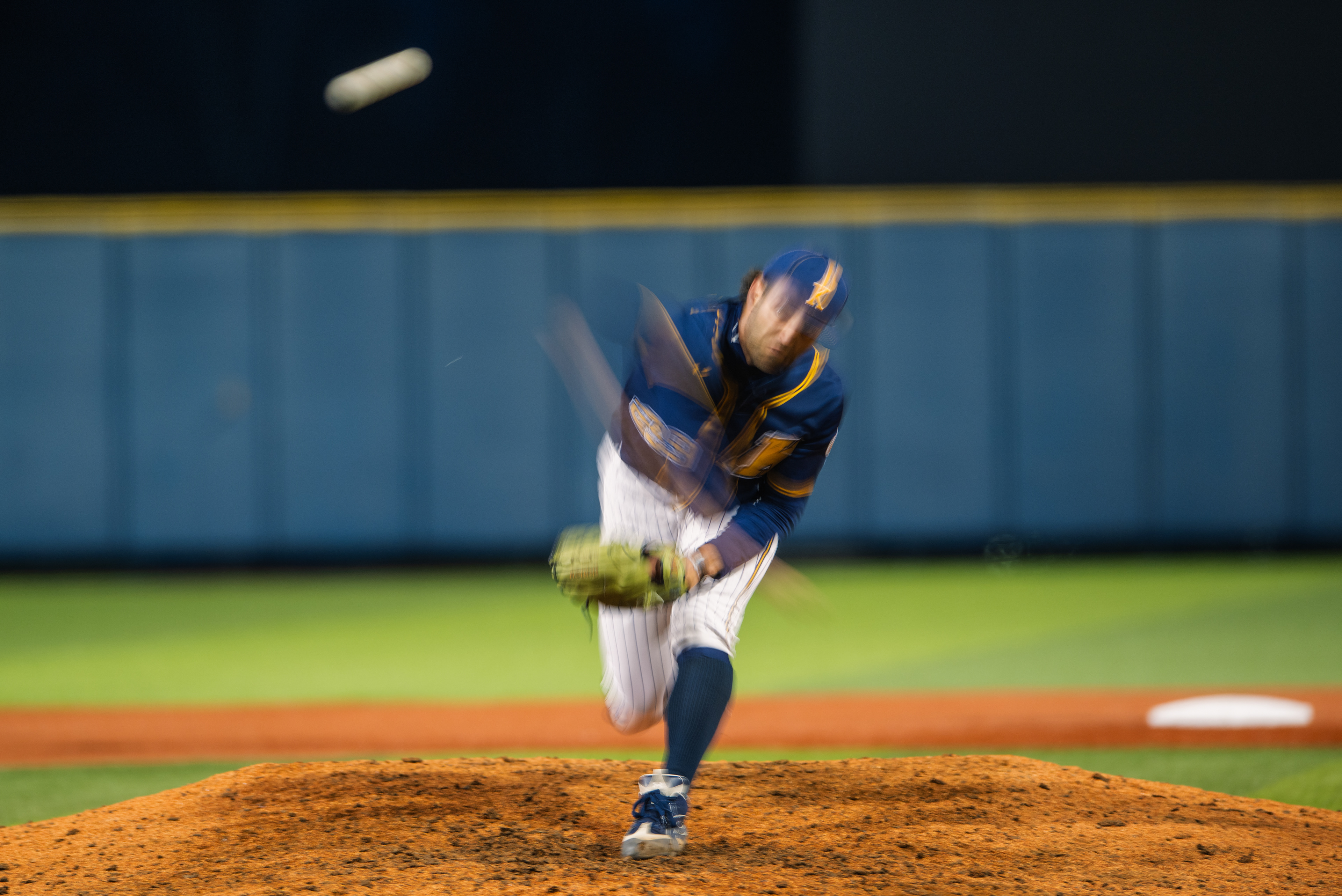 Pure velocity as a slow shutter speed turns a Kent State starter's delivery into motion itself, the pitcher ghosted through the frame while the ball floats free at the top.