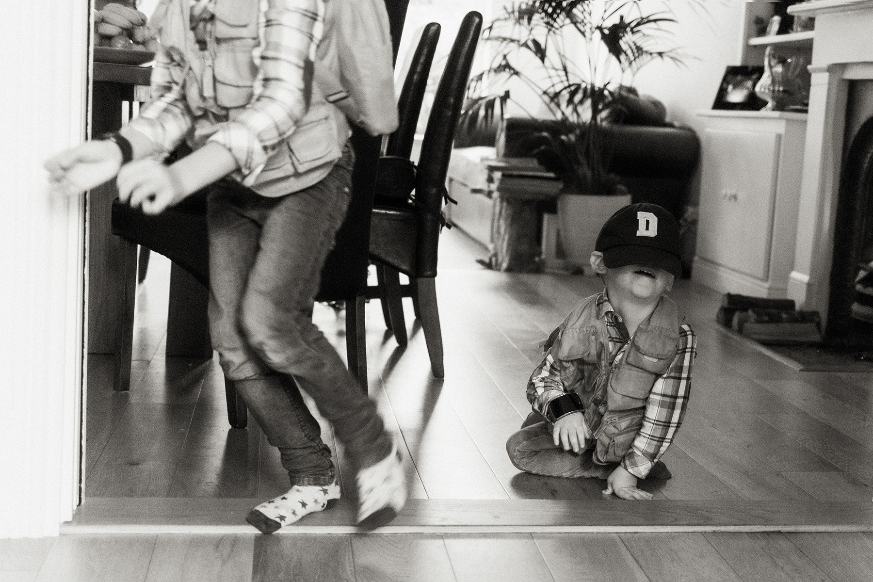 little brother with cap over his eyes while older brother runs away