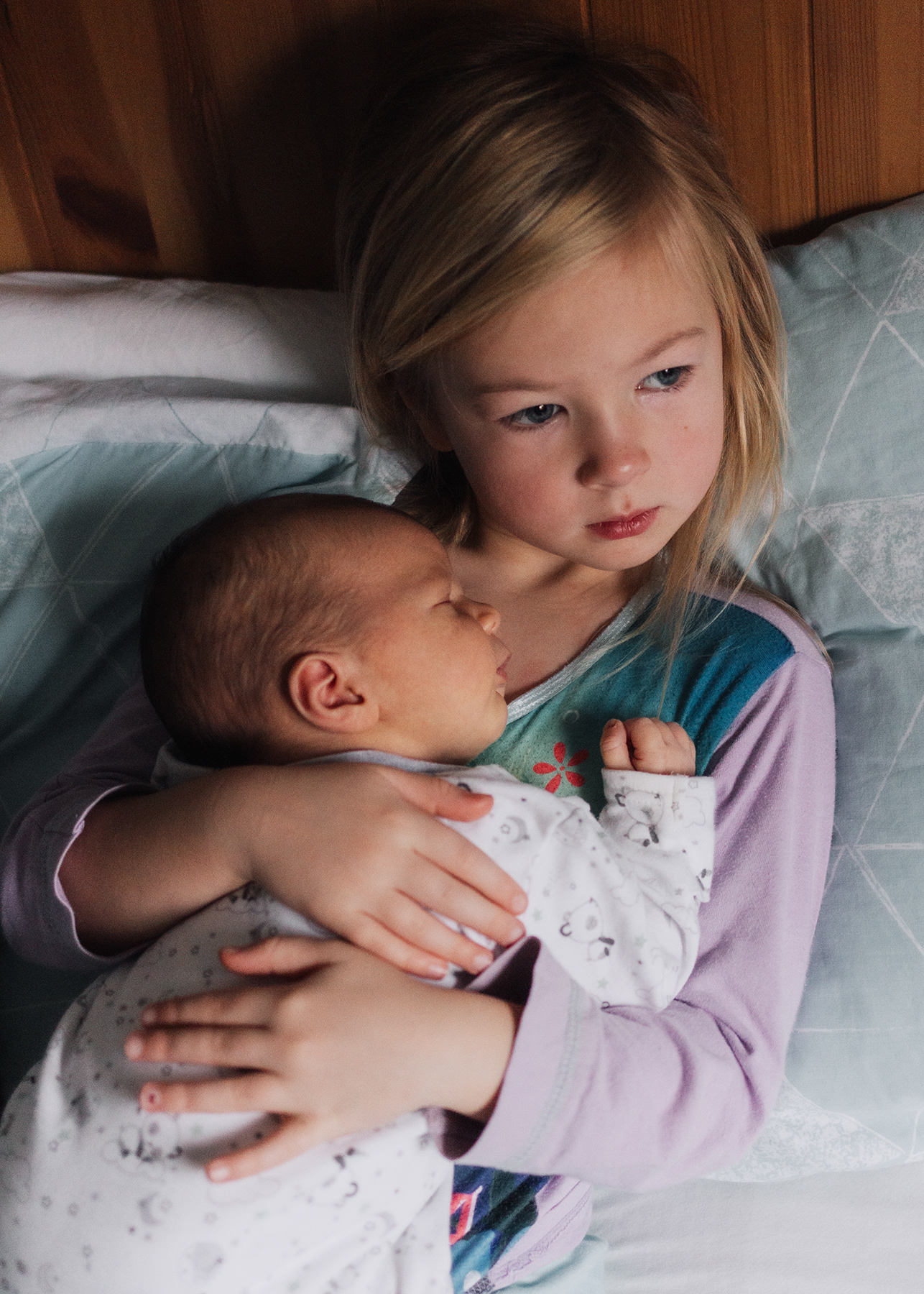 big sister cuddling baby newborn brother