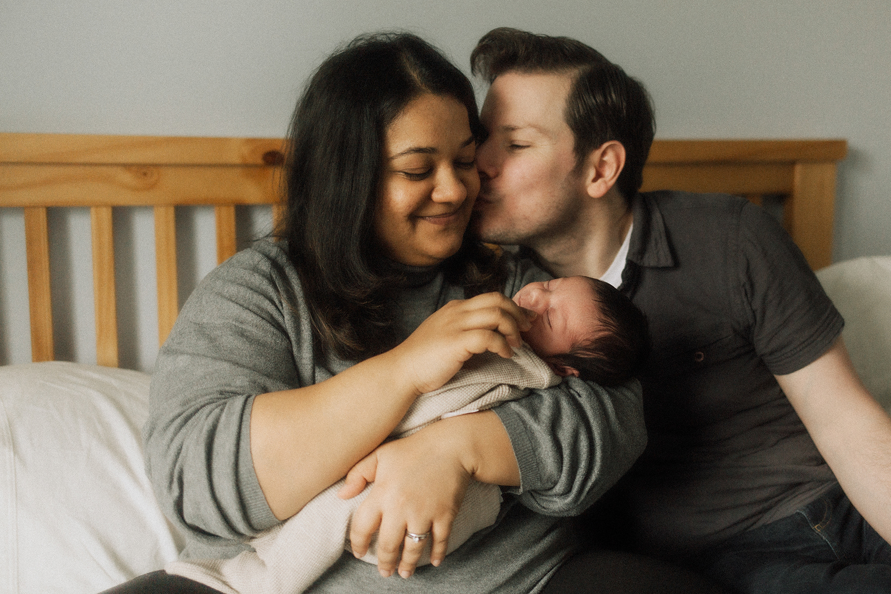 husband kissing wife on the cheek while she holds newborn baby